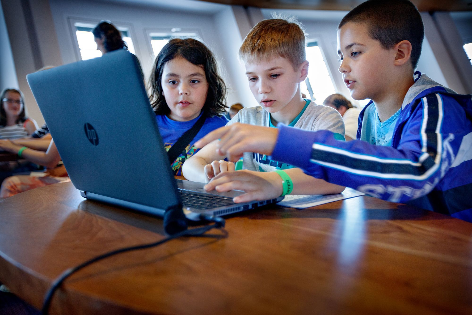 Drie kinderen zitten achter een laptop.