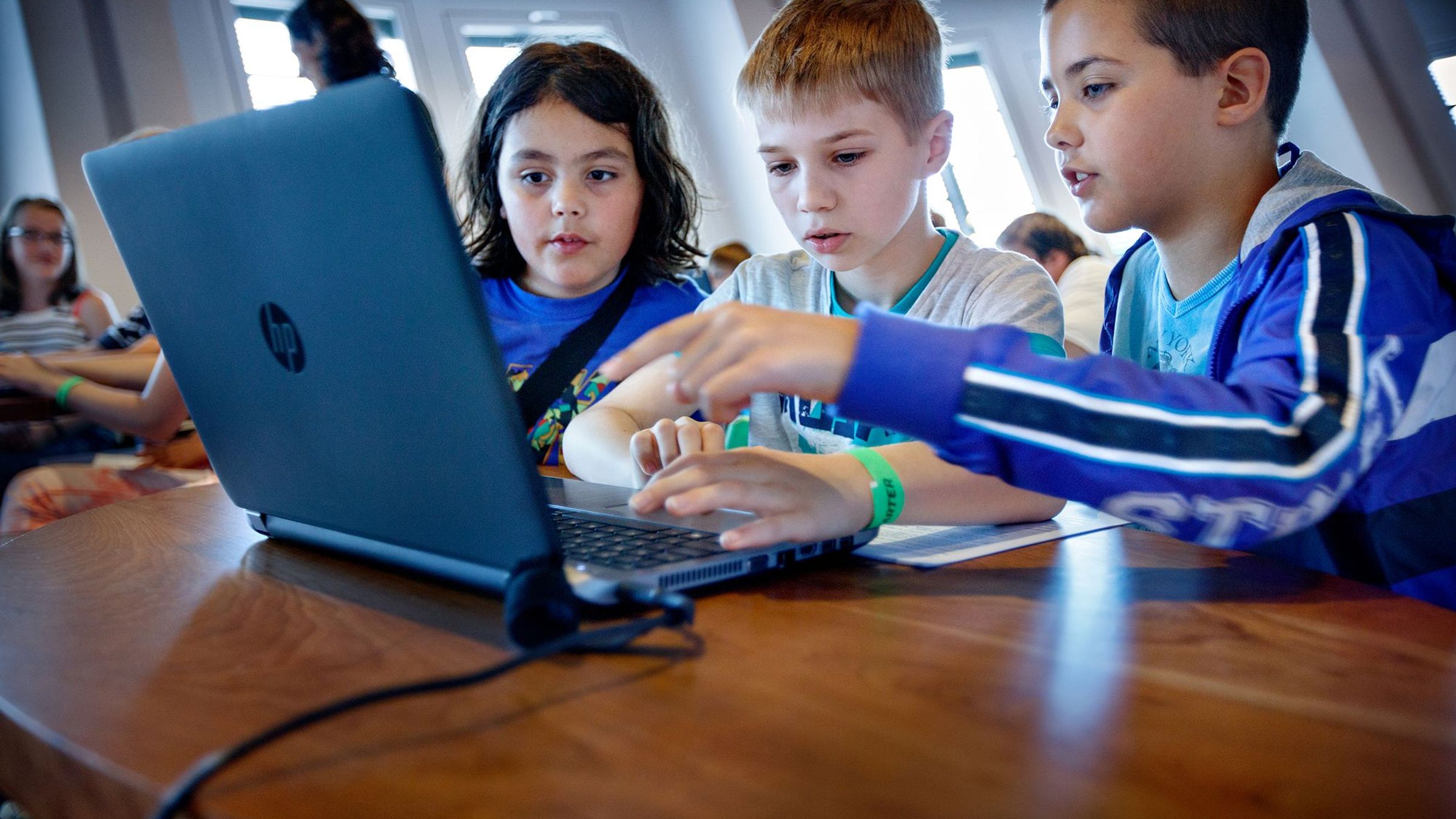Drie kinderen zitten achter een laptop.
