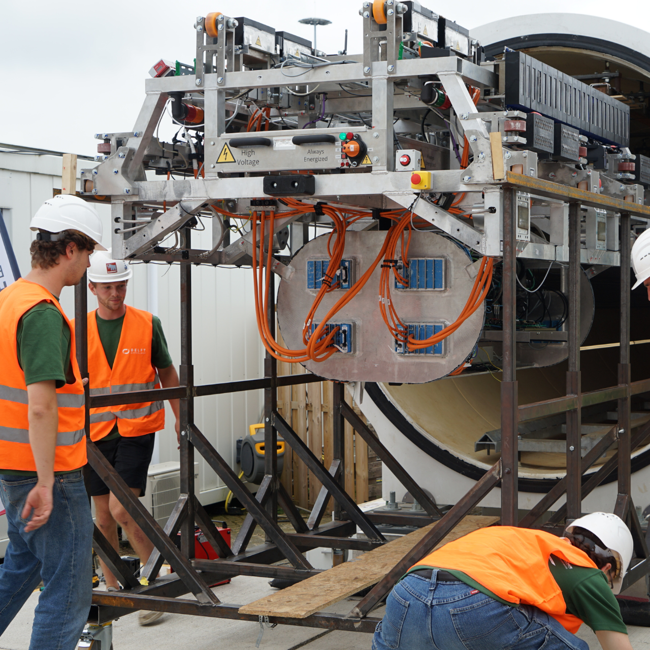 mensen in oranje veiligheidshesjes staan bij een groot apparaat