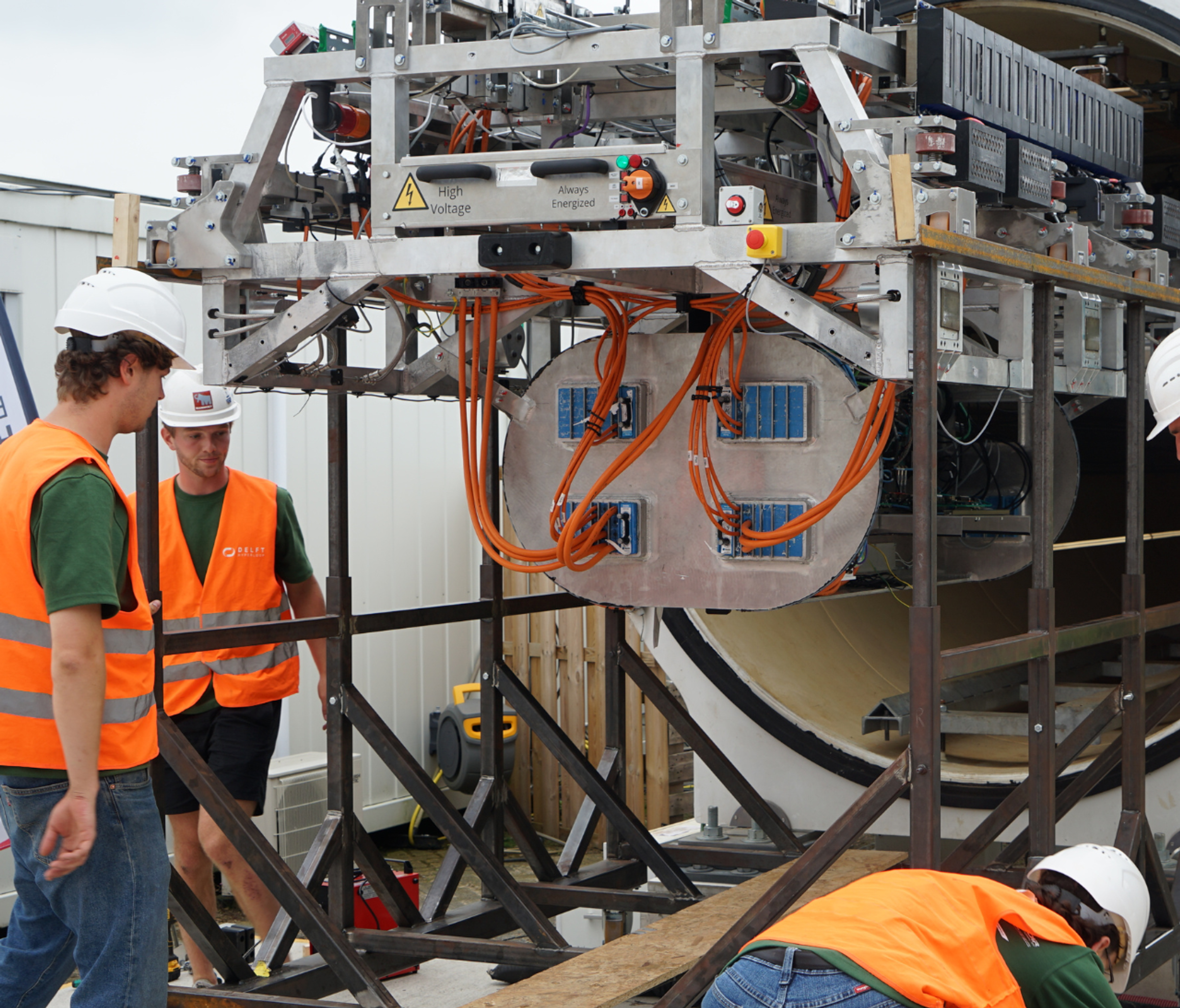 mensen in oranje veiligheidshesjes staan bij een groot apparaat
