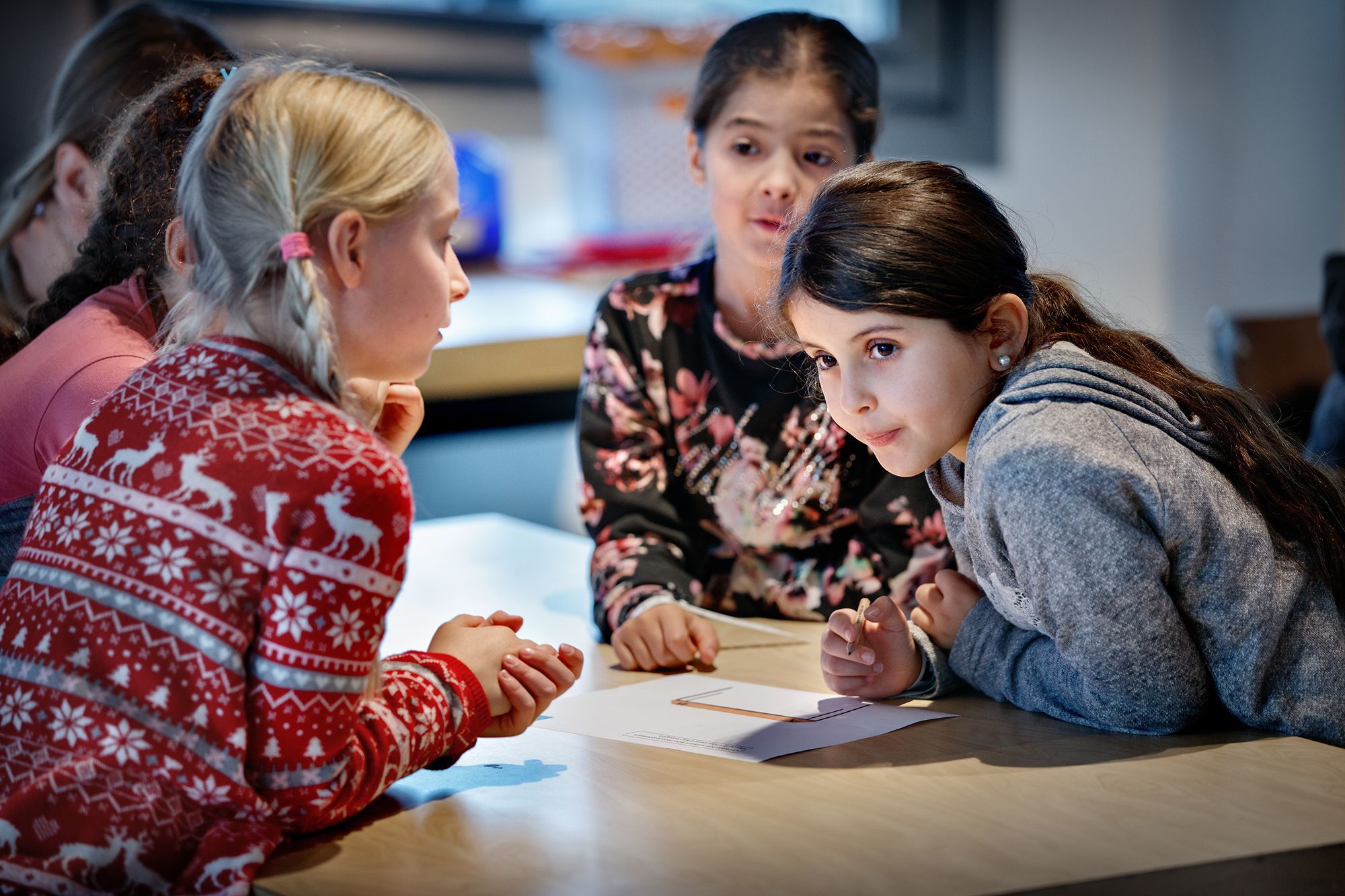 Een groep meisjes zit rondom een tafel met daarop papier.