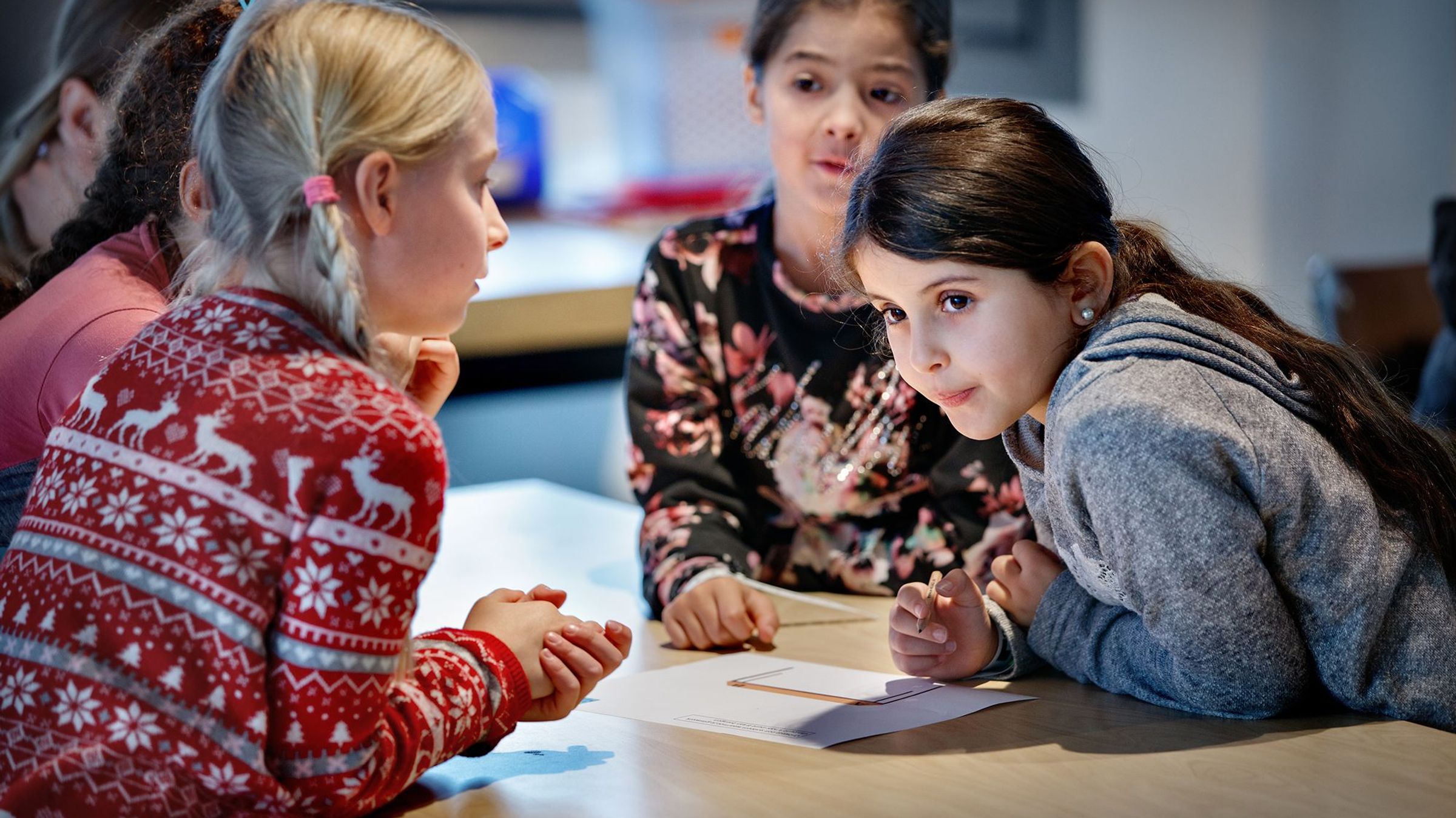Een groep meisjes zit rondom een tafel met daarop papier.