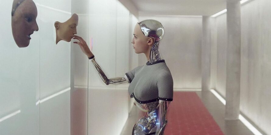 A female robot is looking at a human mask.
