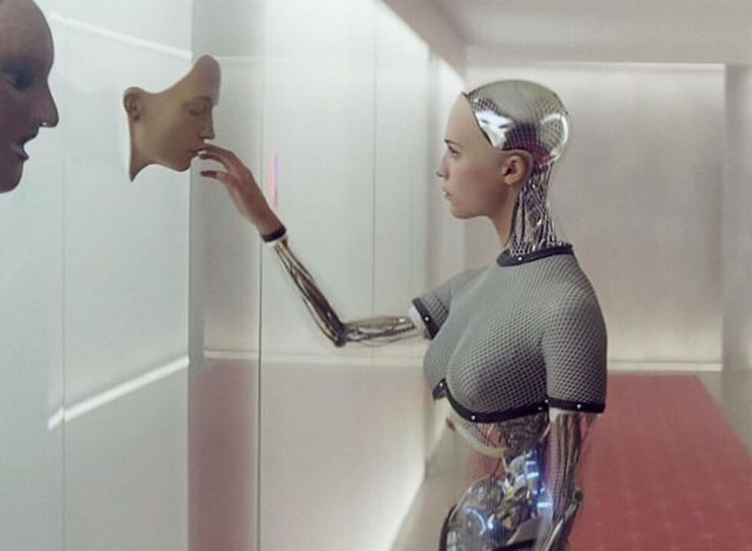 A female robot is looking at a human mask.