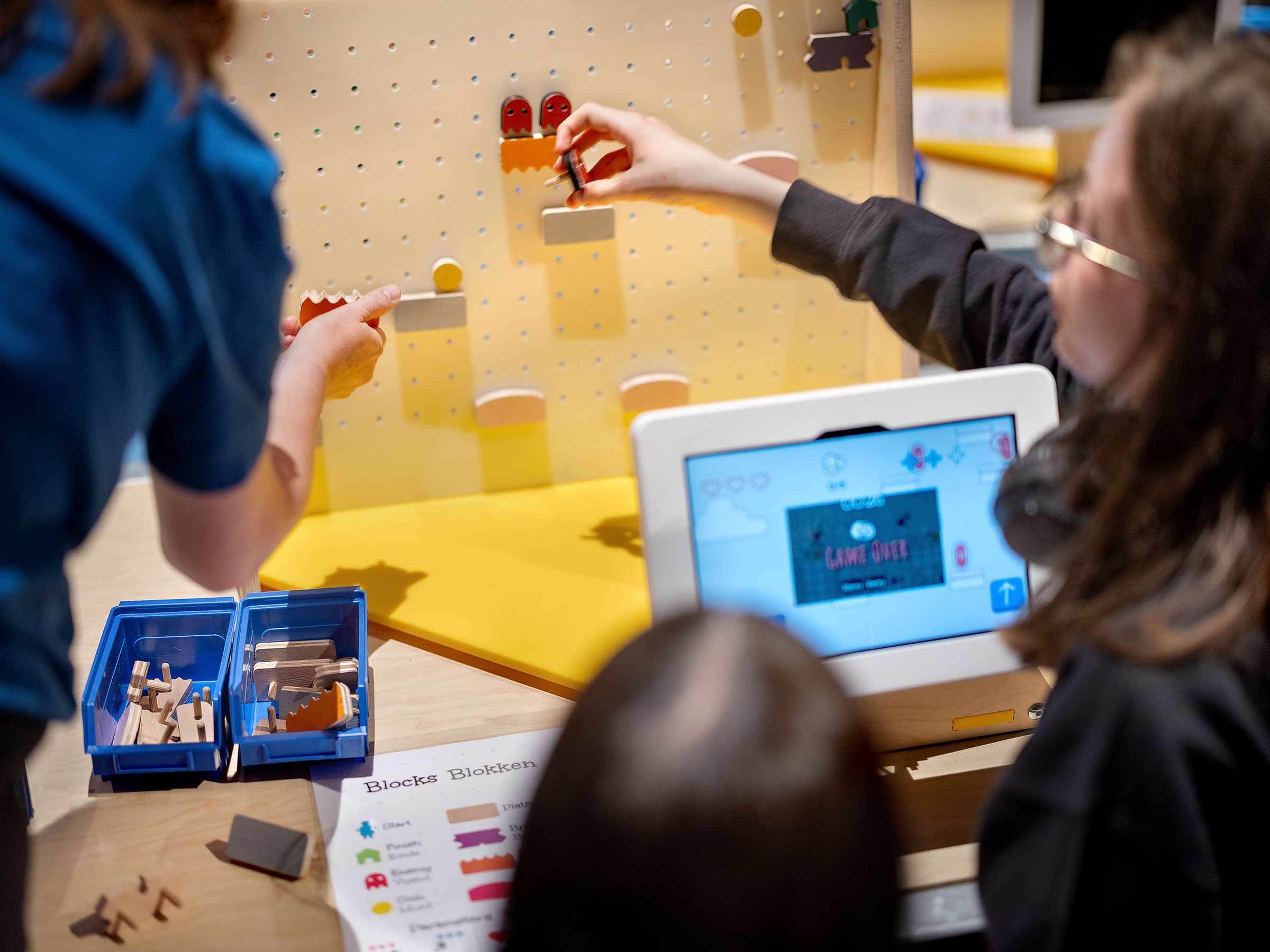 Drie mensen staan bij een tablet en plaatsen figuurtjes op een muur.