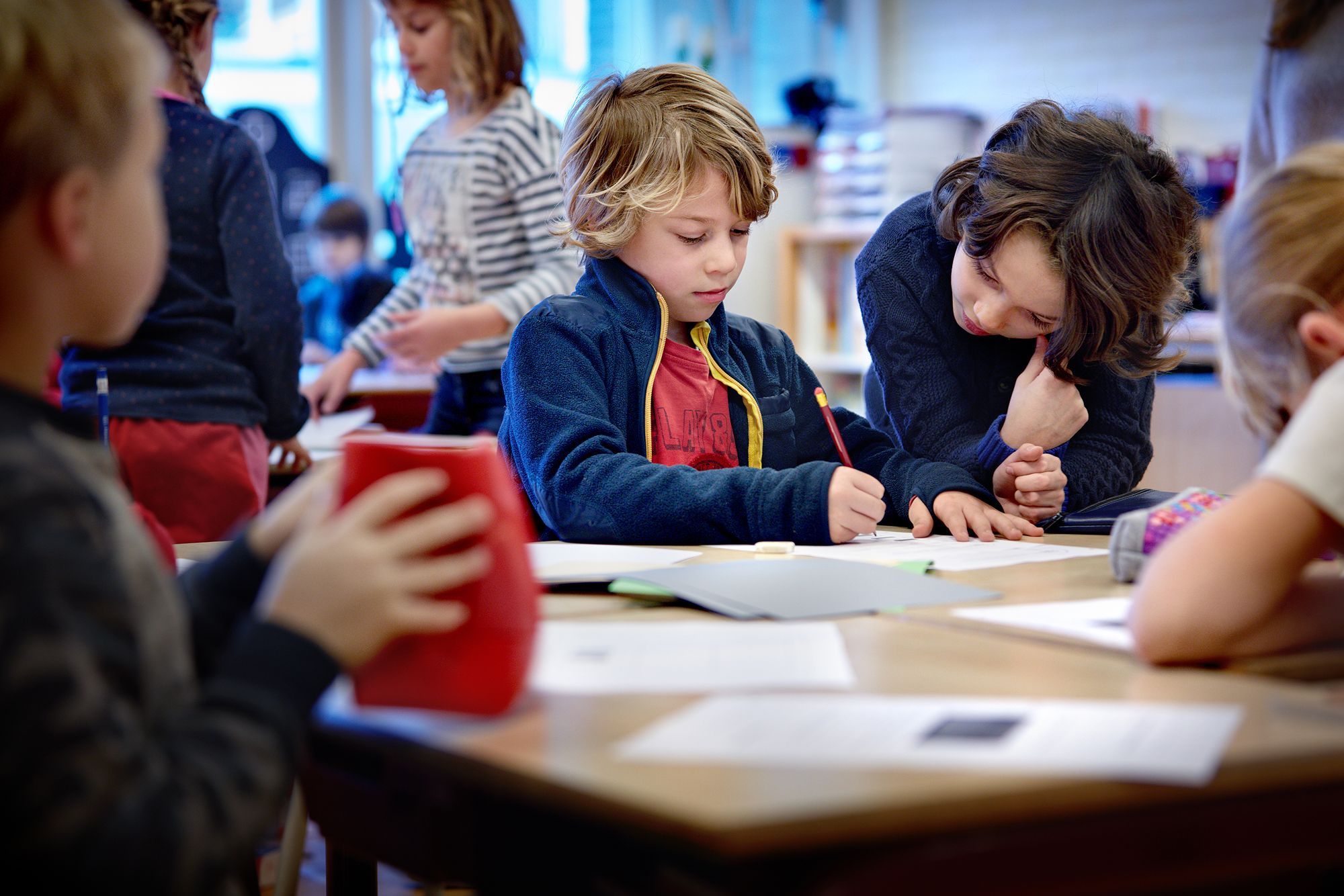 Een jongen tekent op een papier, een andere jongen kijkt toe.