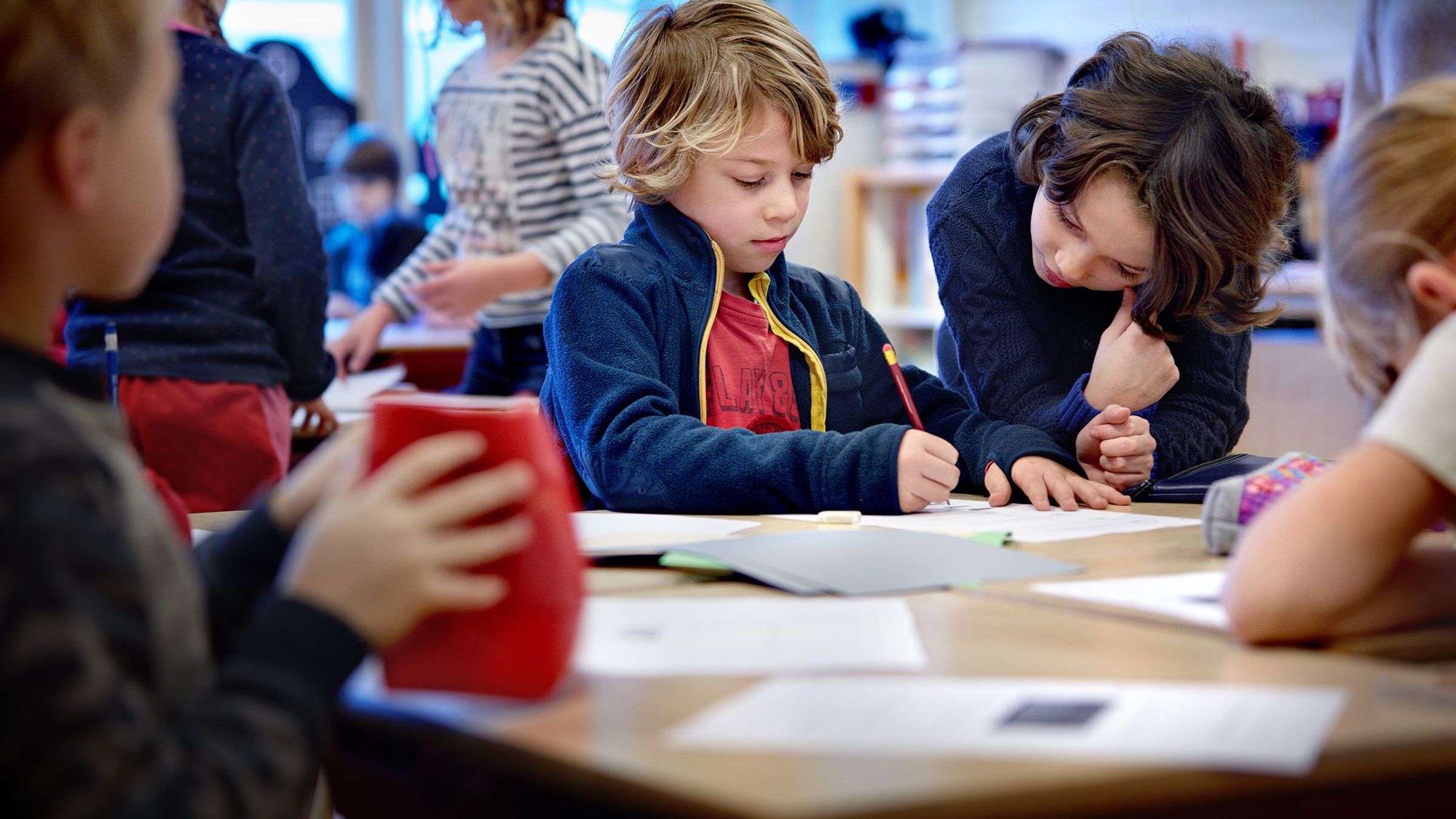 Een jongen tekent op een papier, een andere jongen kijkt toe.