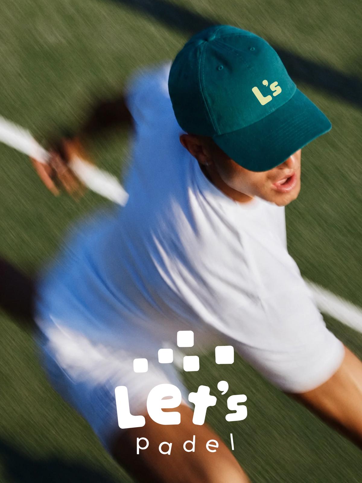 A player in a cap and white shirt seen from behind on a padel court.