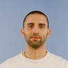 A man with a beard is wearing a beige sweatshirt with the words "UNKNOWN BASICS" on it.