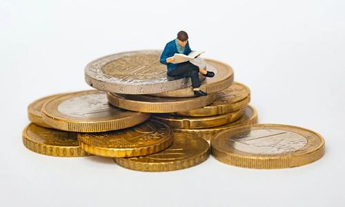 man reading a book and standing on a pile of money