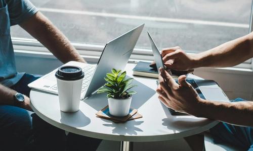 doi oameni care stau deasupra unei masute la o cafea cu laptopuri pe masa si discuta