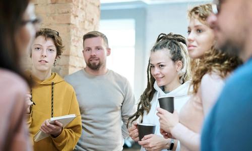 people standing around with notebooks and coffee listening to someone