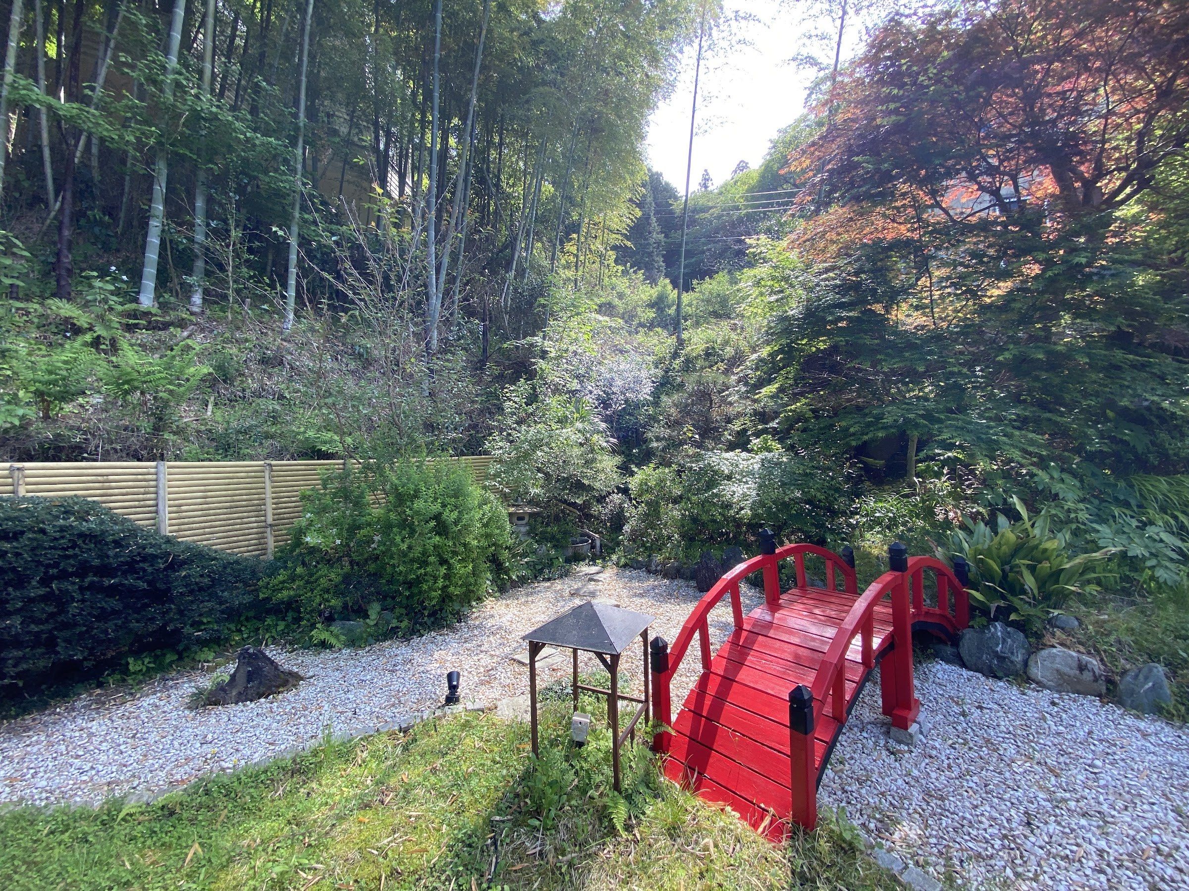 A red footbridge crossing a quiet wooded garden