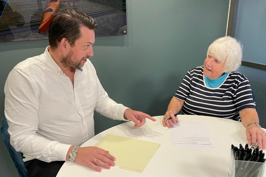 Eiendomsmegler og kunde sitter ved et bord i et møterom. Foto.