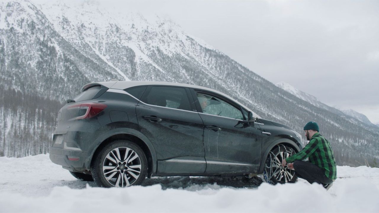 Man doing his snow chains on his car in the mountains.