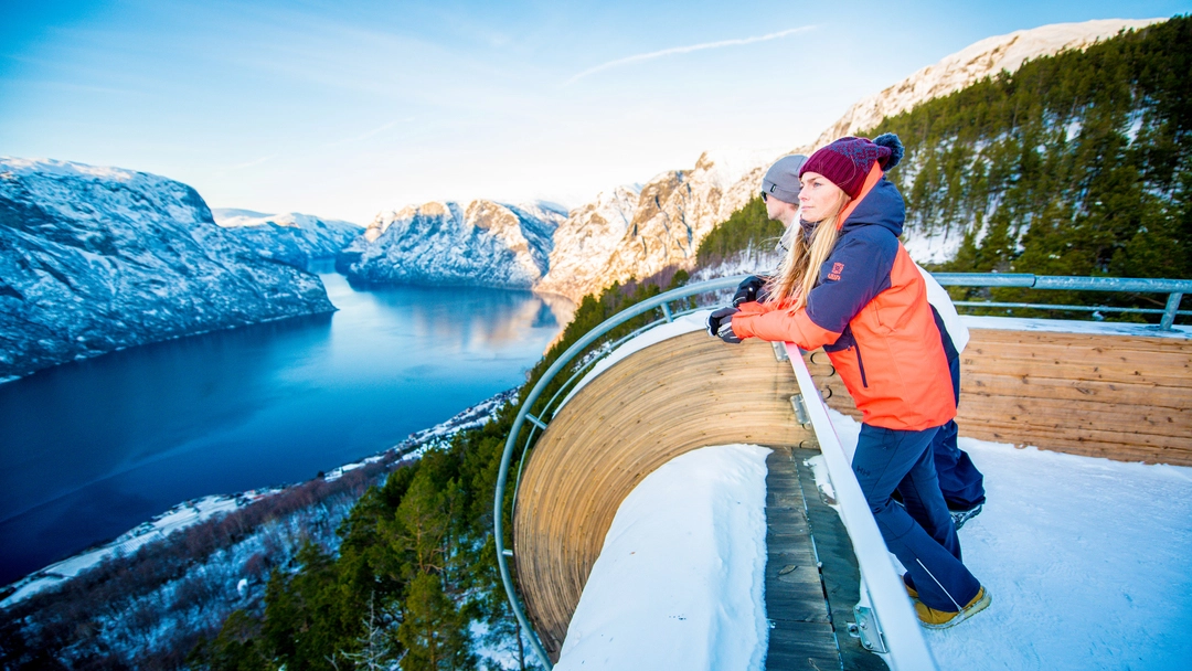 Frau am Aussichtspunkt Stegastein über dem Aurlandsfjord im Winter Frau genießt spektakuläre Panoramaaussichten von der schneebedeckten Aussichtsplattform Stegastein über den Aurlandsfjord und dramatische norwegische Berge - als Zusatzoption zur Norway in a Nutshell Wintertour verfügbar