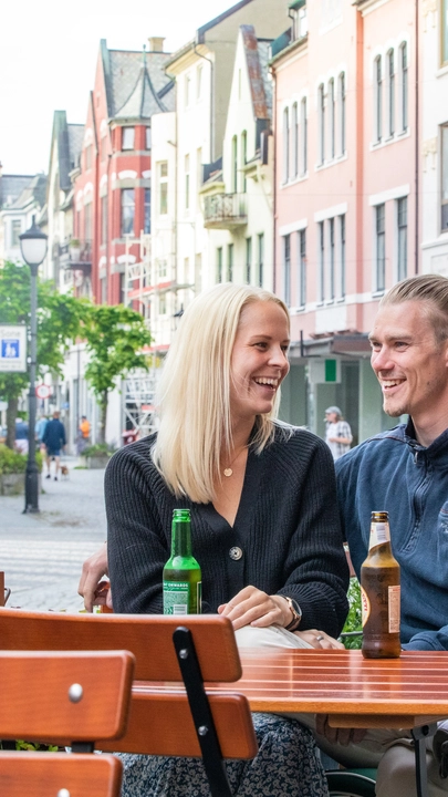 Kafékultur i Kongens gate, Ålesund Par nyter noe å drikke på en kafé i Kongens gate, Ålesund. Opplev lokal kultur under ditt Ålesund-besøk omgitt av vakre jugendstilbygninger.