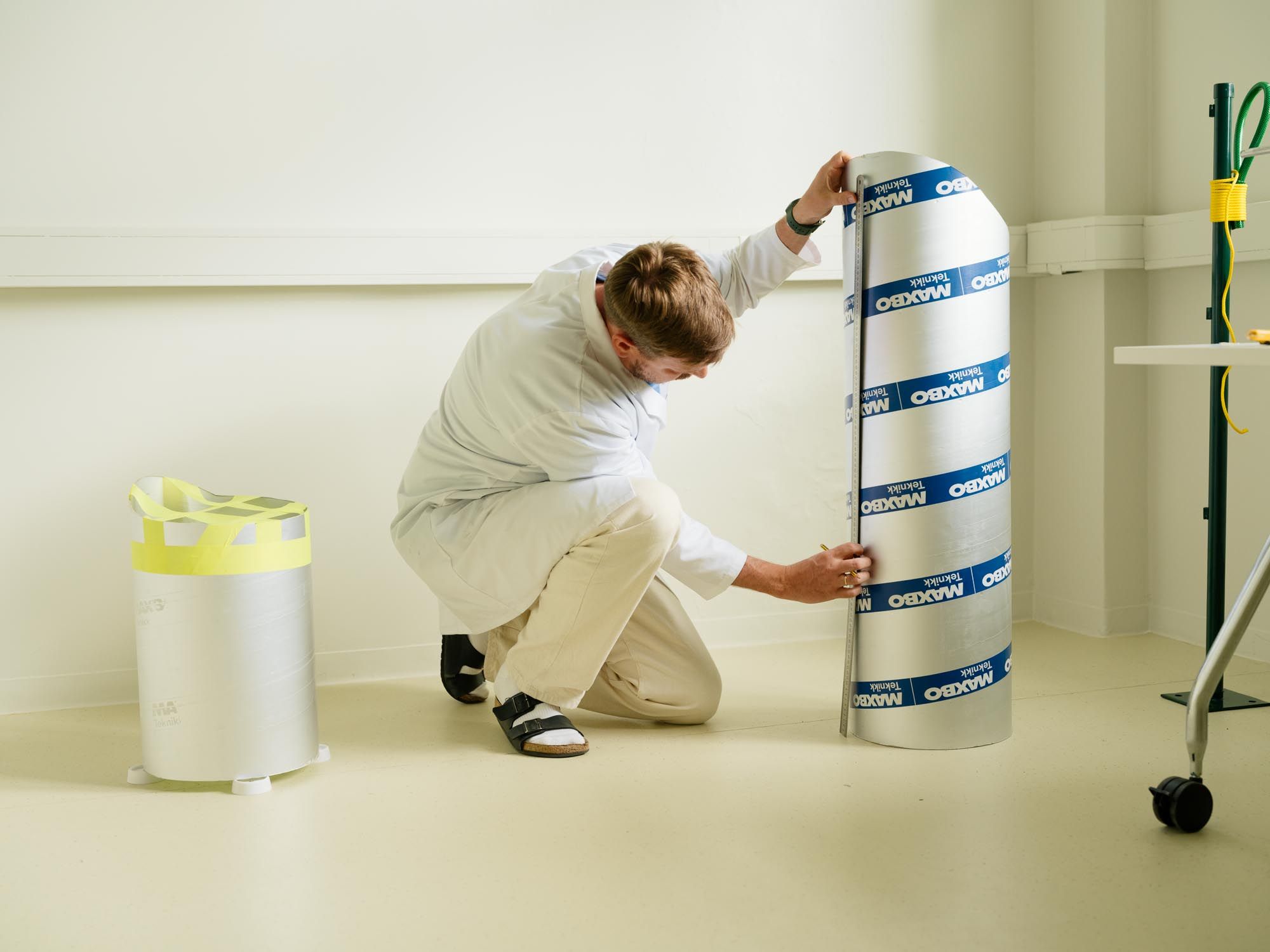 Designer in white coat measuring on a large ventialtion tube with metal ruler