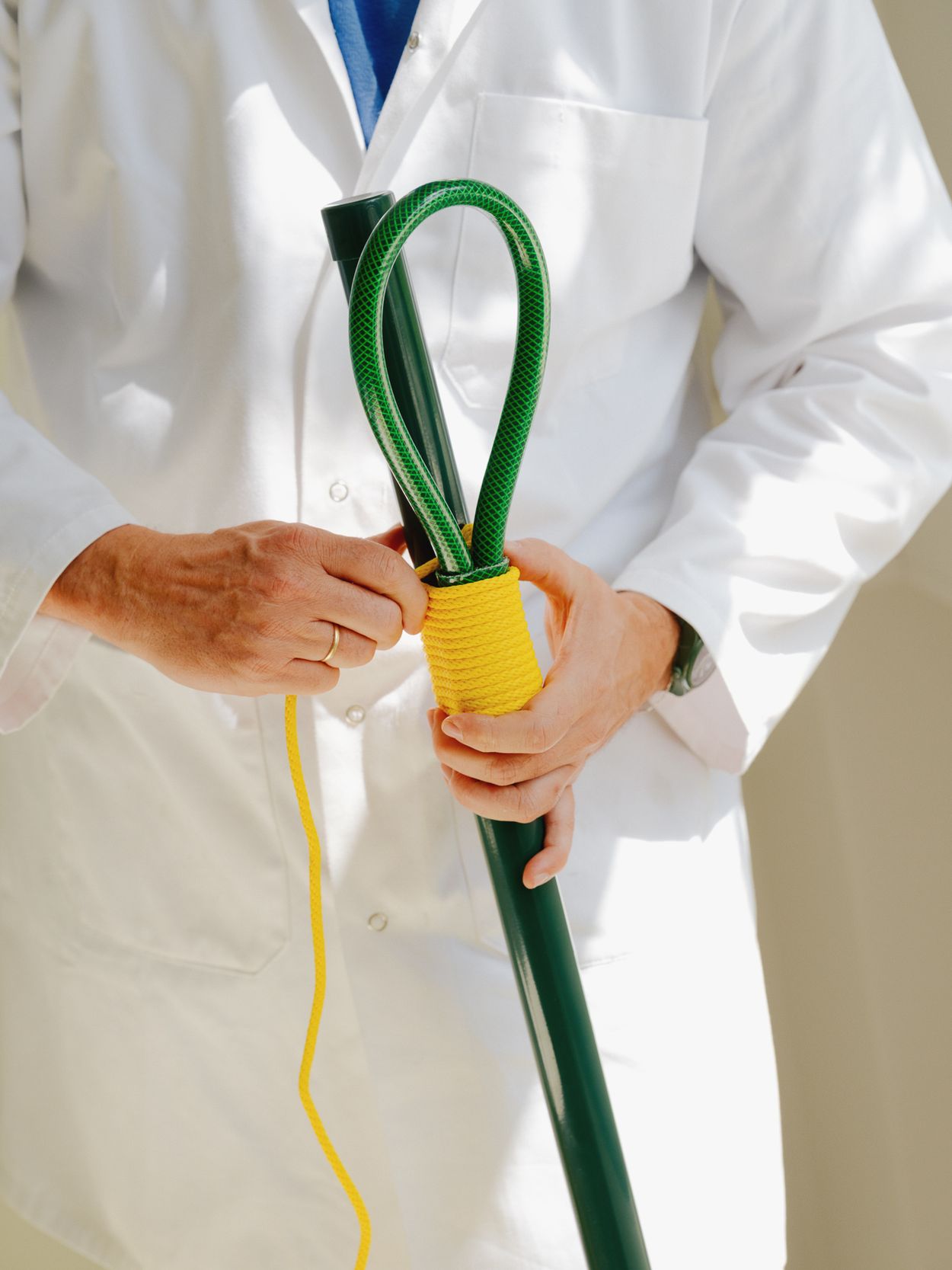 designer with white coat tying a yellow rope to fasten a cut off garden hose that will become a coat rack