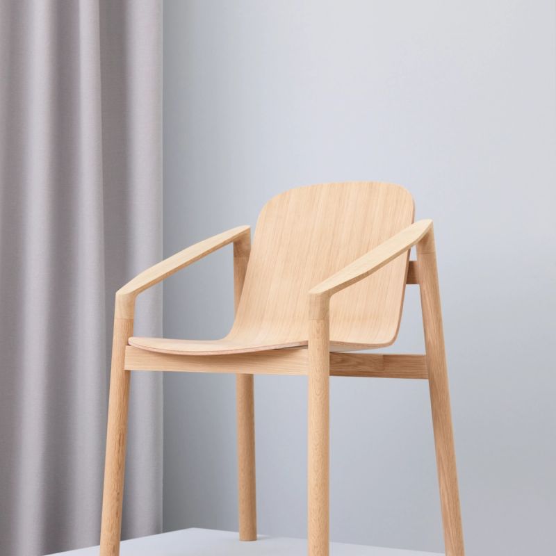 Tjøme Chair, a wooden chair standing on a white pedestal with white walls and a white curtain in the background