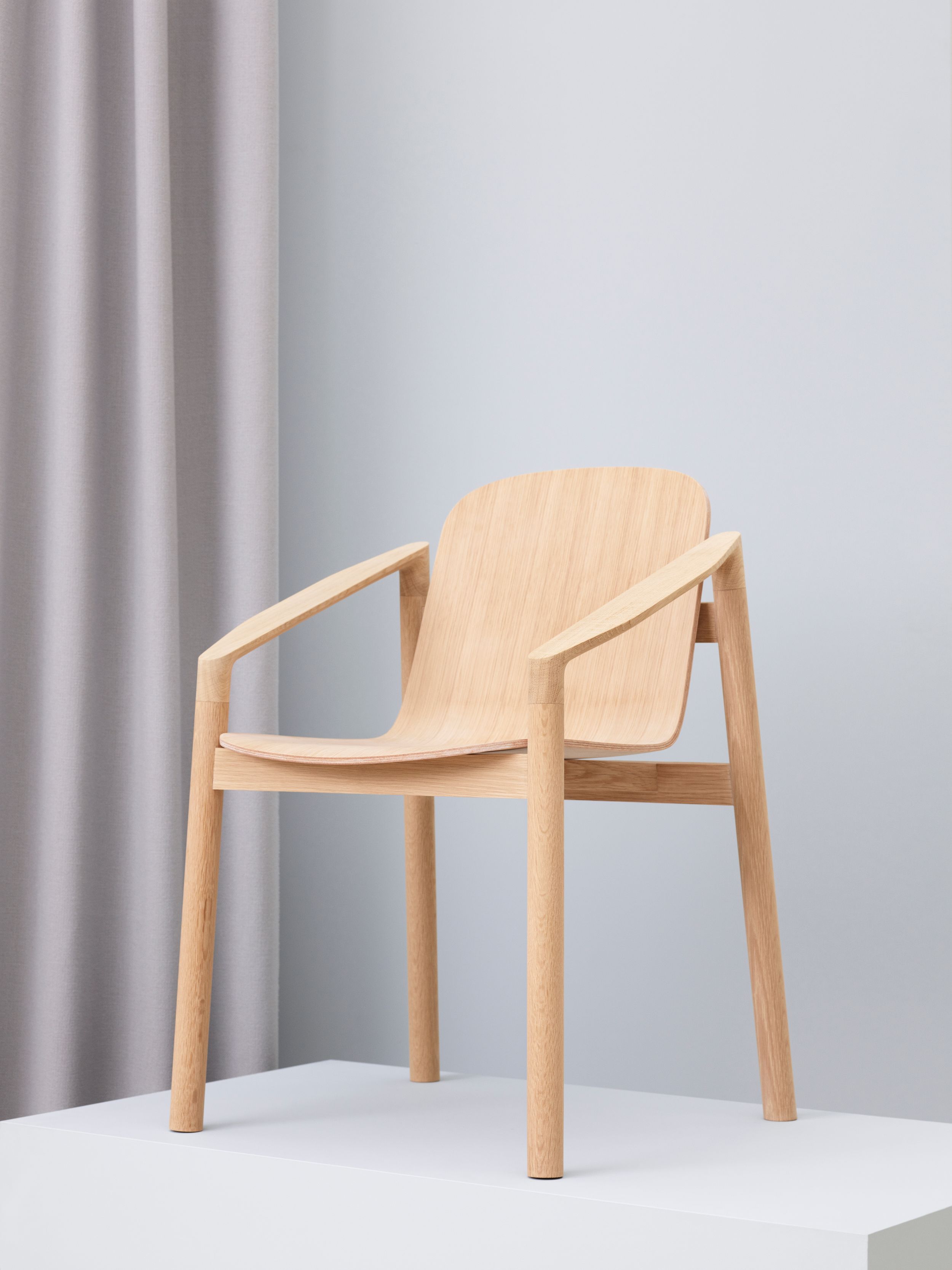 Tjøme Chair, a wooden chair standing on a white pedestal with white walls and a white curtain in the background