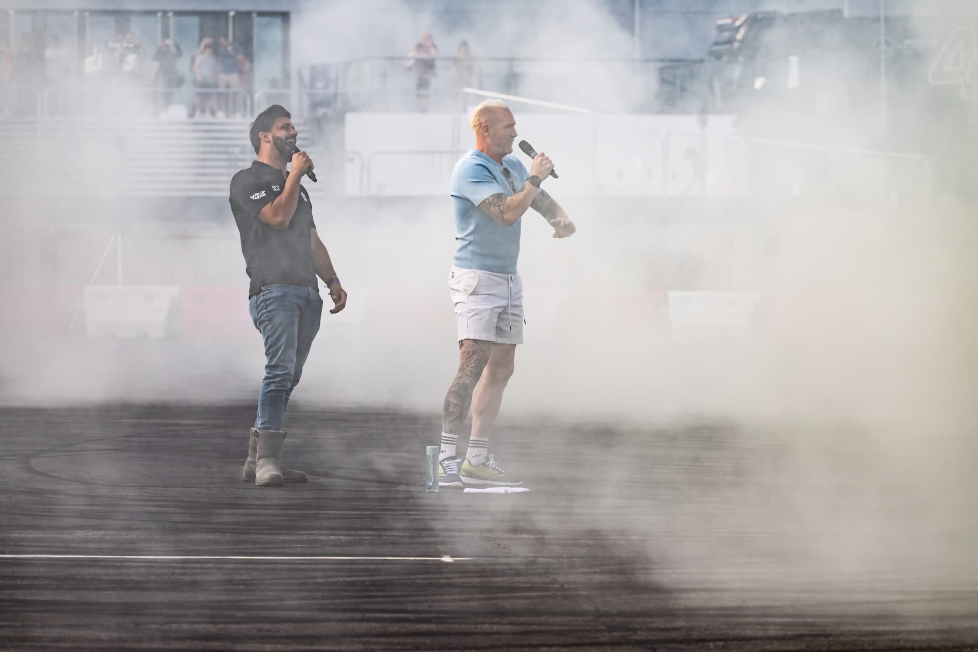 Two presenters with microphones standing in a cloud of tyre smoke