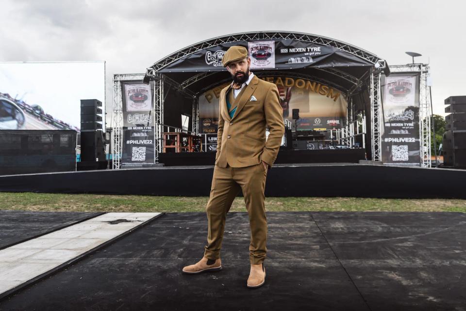 Sam in a brown suit in front of the main stage at a car show