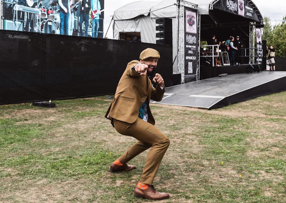 Sam in a tweed suit striking a pose on the grass in front of a stage