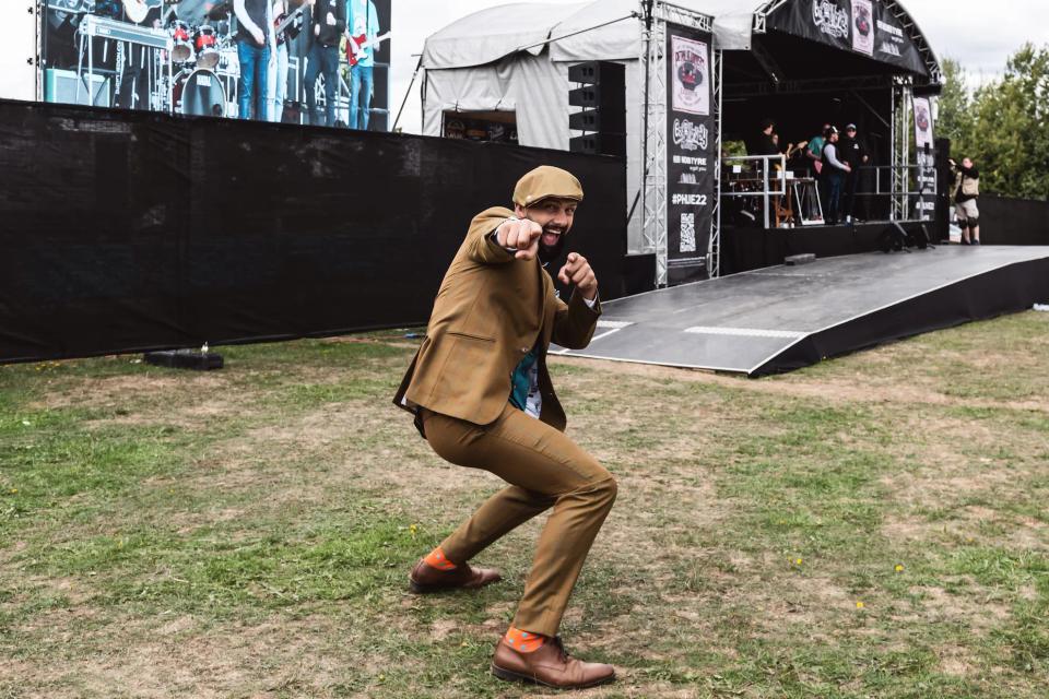 Sam in a tweed suit striking a pose on the grass in front of a stage