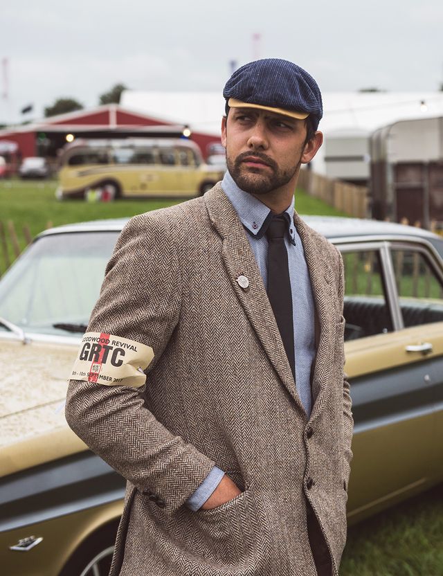 Sam in a tweed jacket and flat cap beside a classic car