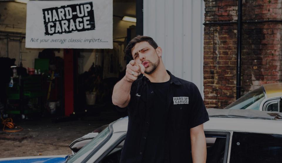 Sam Hard pointing at the camera outside the Hard Up Garage workshop
