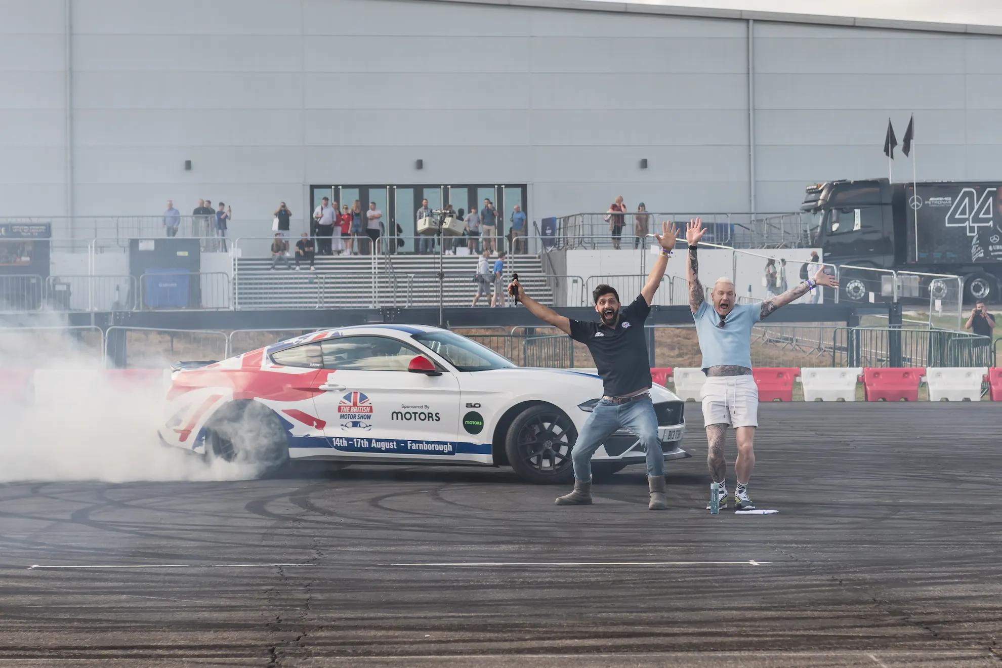 Sam and a driver celebrating beside a drifting car in tyre smoke