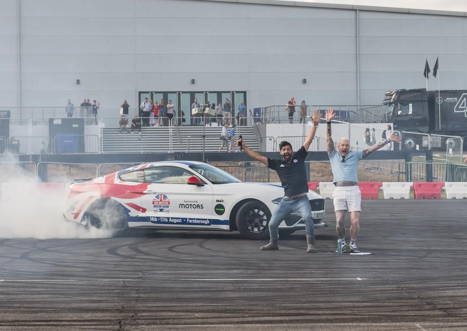 Sam and a driver celebrating beside a drifting car in tyre smoke