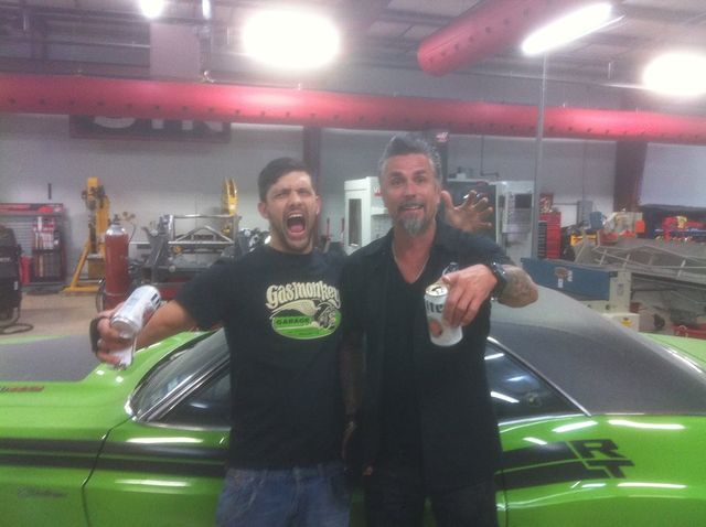 Sam and a friend laughing with drinks beside a green car