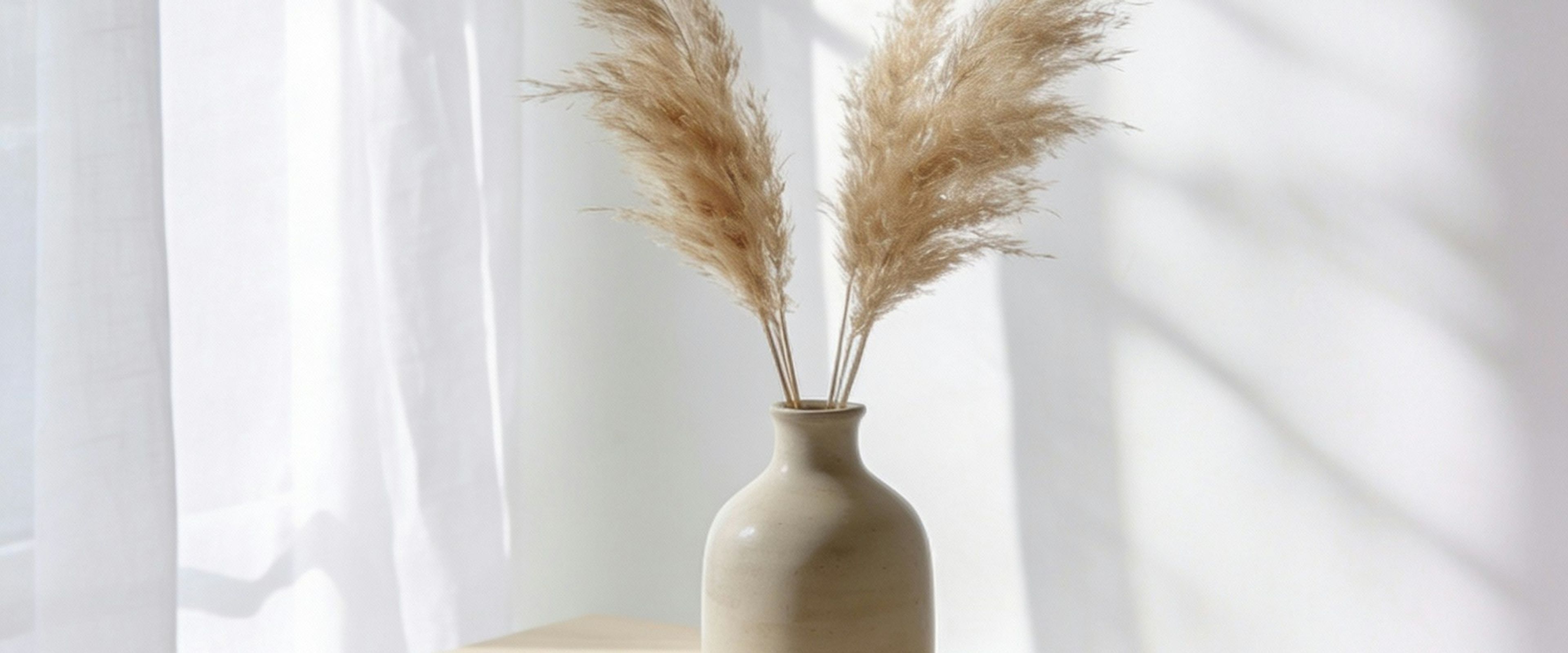 Dried grasses in a ceramic vase on a sunlit shelf