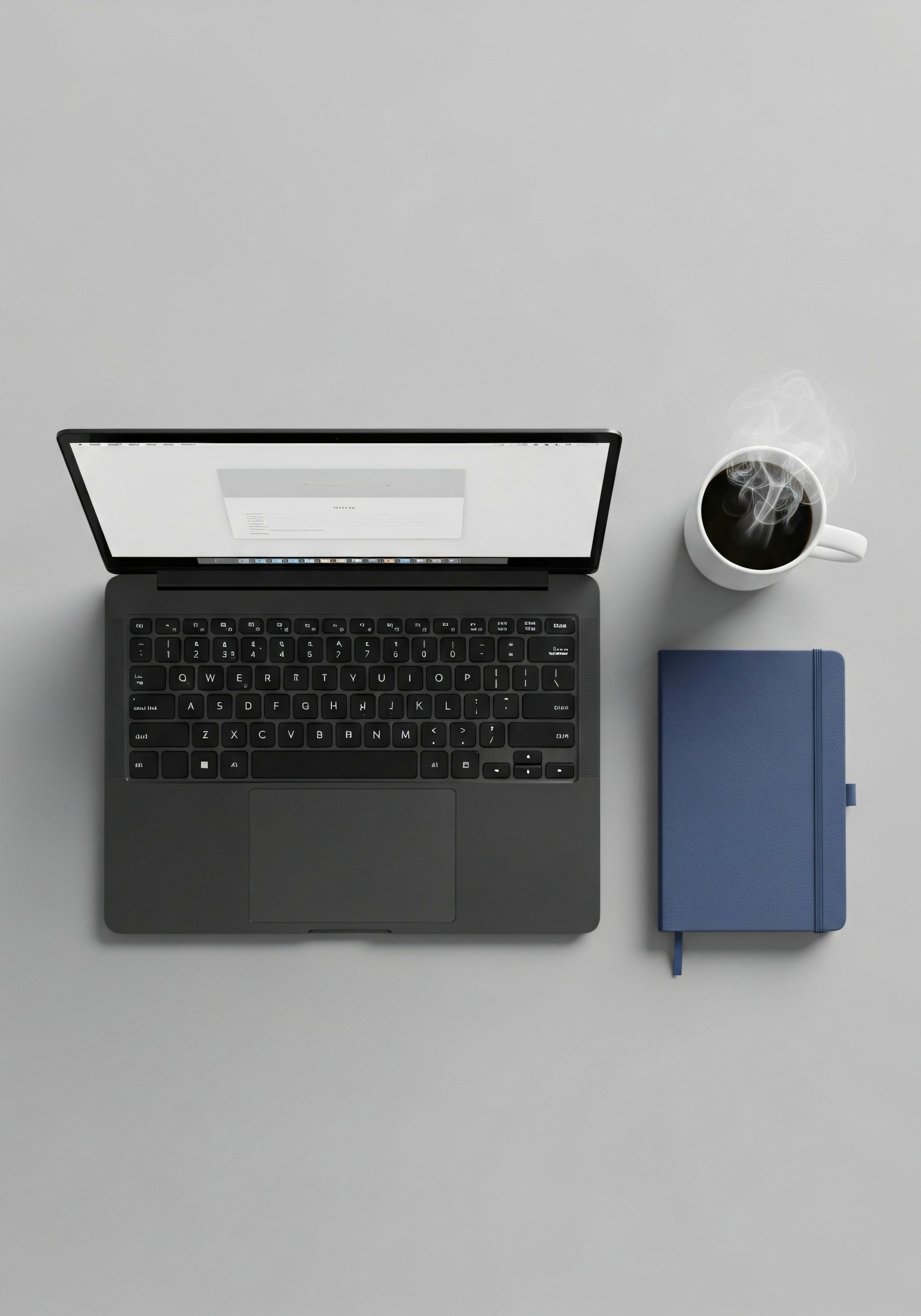 A laptop, notebook and coffee on a grey desk