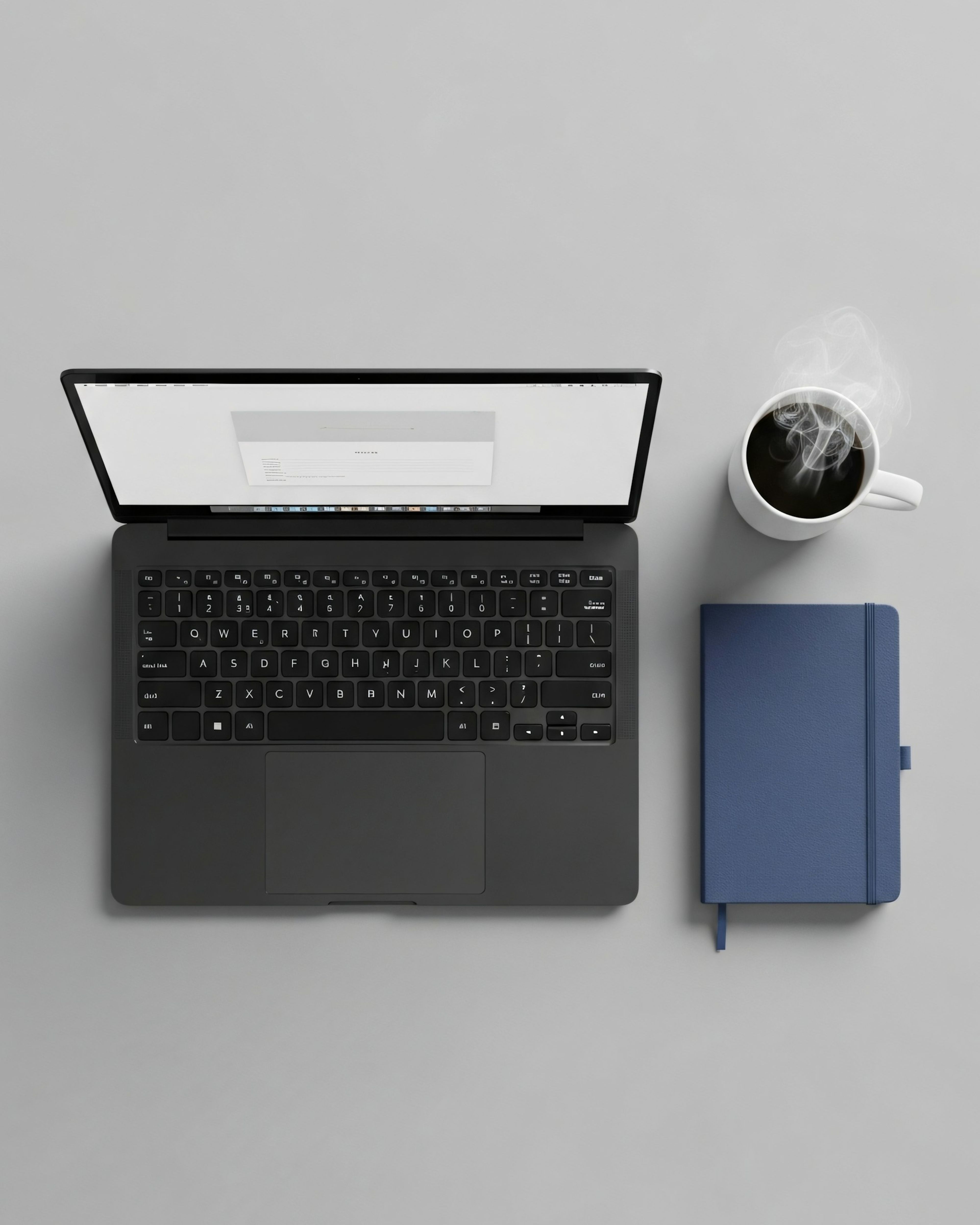 A laptop, notebook and coffee on a grey desk