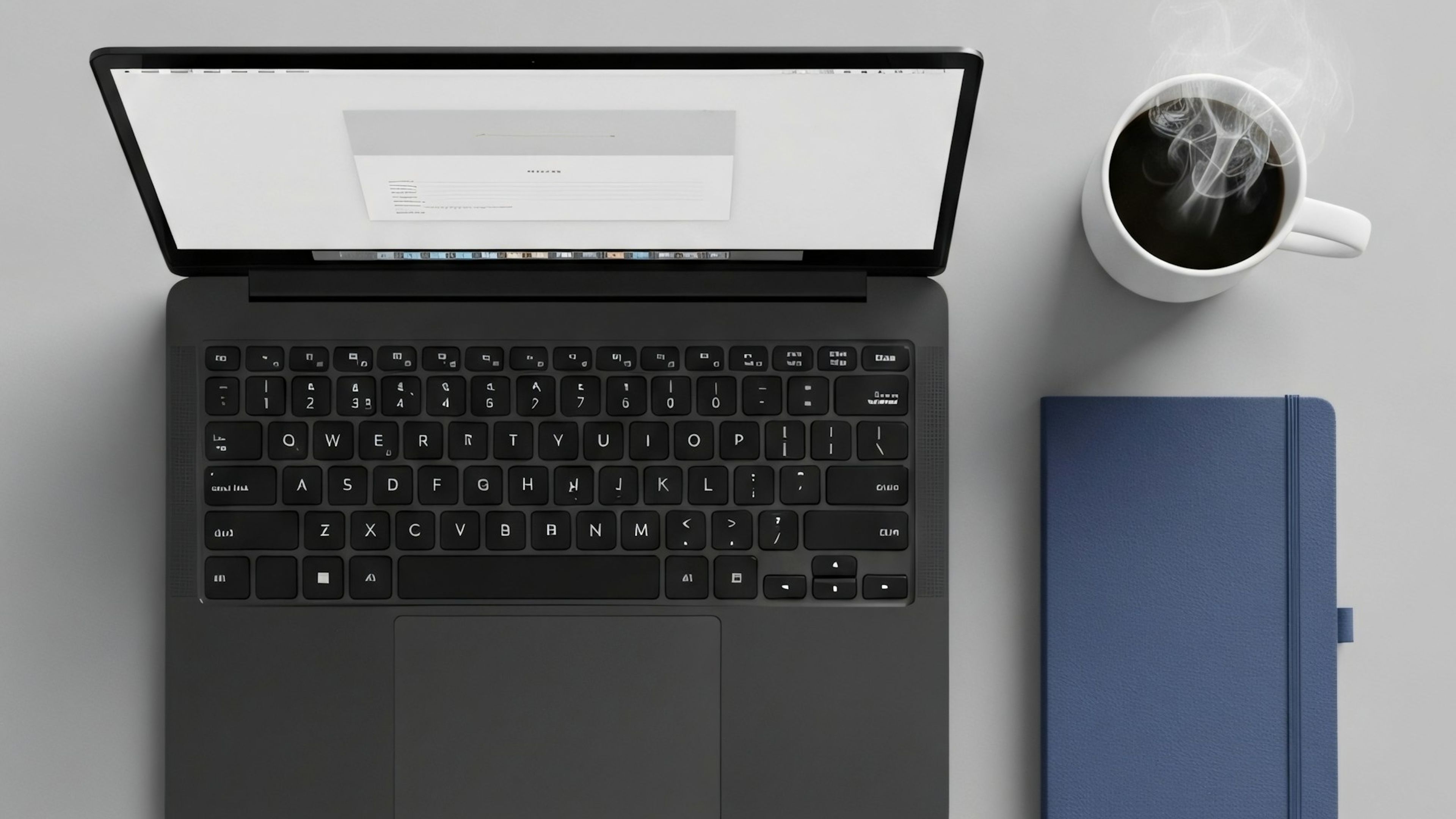 A laptop, notebook and coffee on a grey desk
