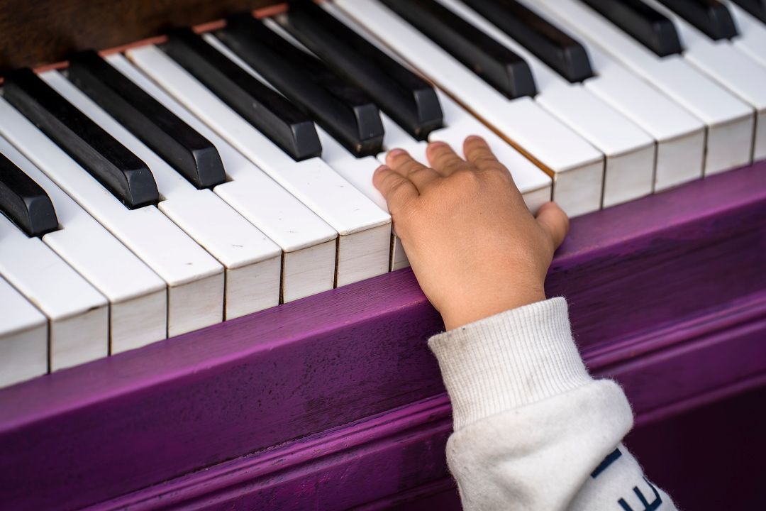 Bildet viser en barnehånd som spiller på et lilla piano.