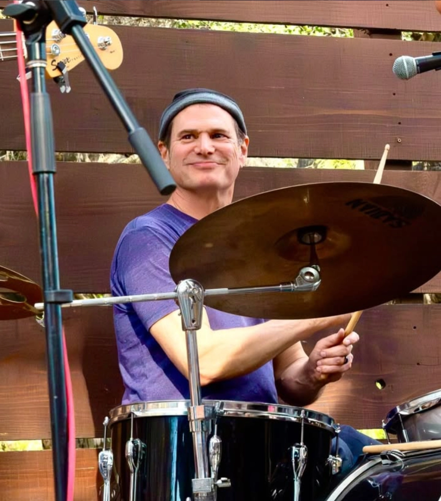 Paul smiling behind the drum kit at an outdoor show.