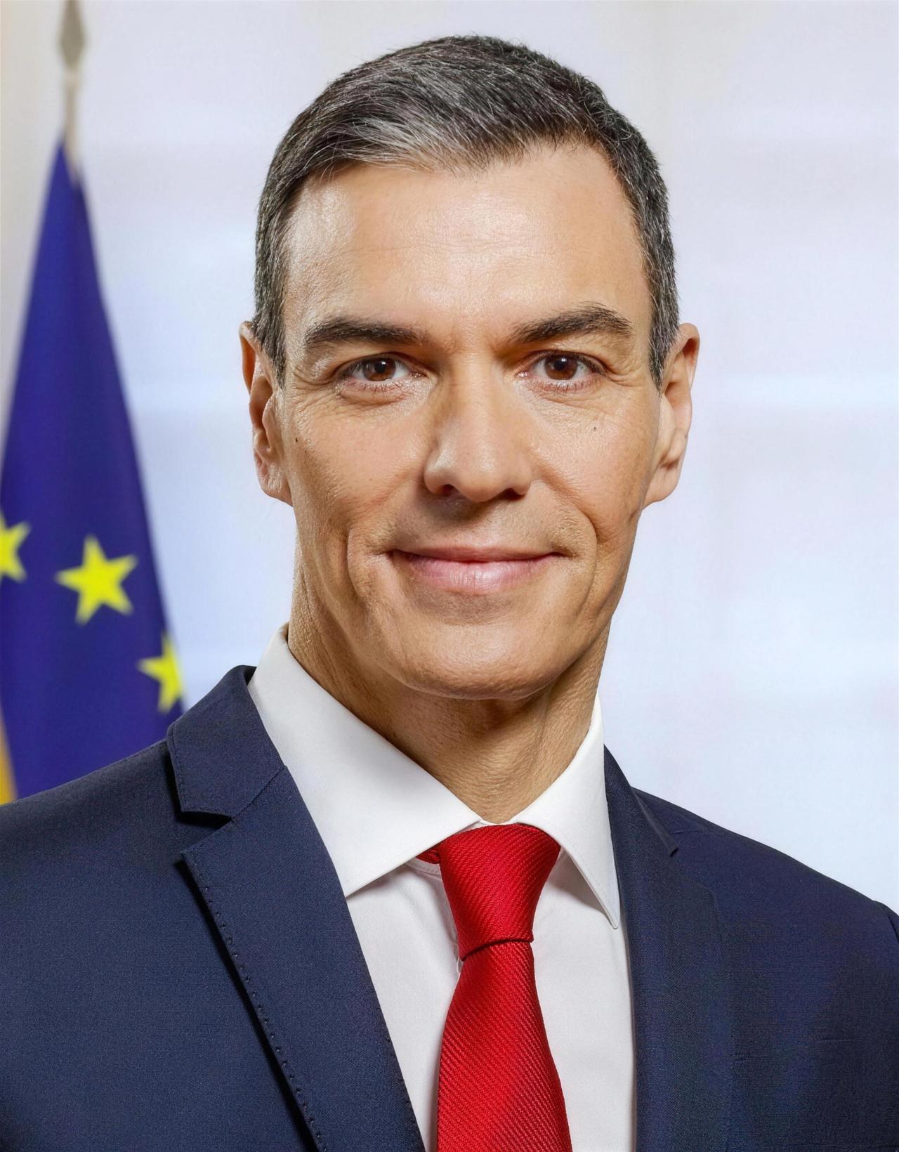 Retrato de un hombre de traje azul marino y corbata roja frente a la bandera de la Unión Europea