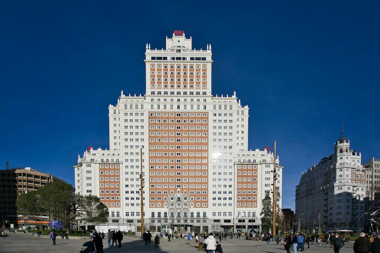 Plaza pública con edificio art déco de fachada blanca y naranja, rodeado de personas y otros inmuebles en arquitectura