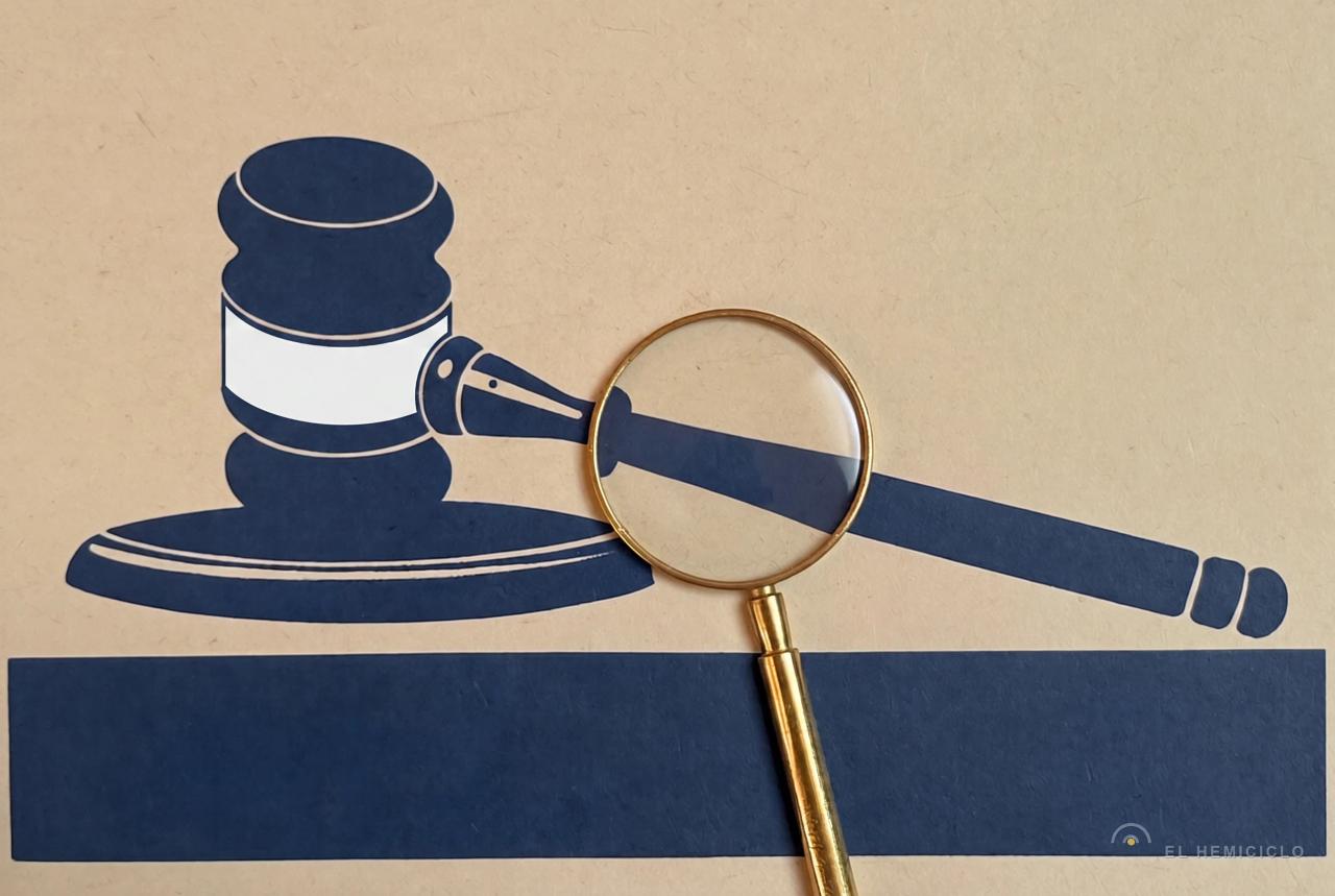 Martillo de juez en azul y blanco junto a lupa dorada sobre fondo beige, simbolizando análisis judicial o investigación legal