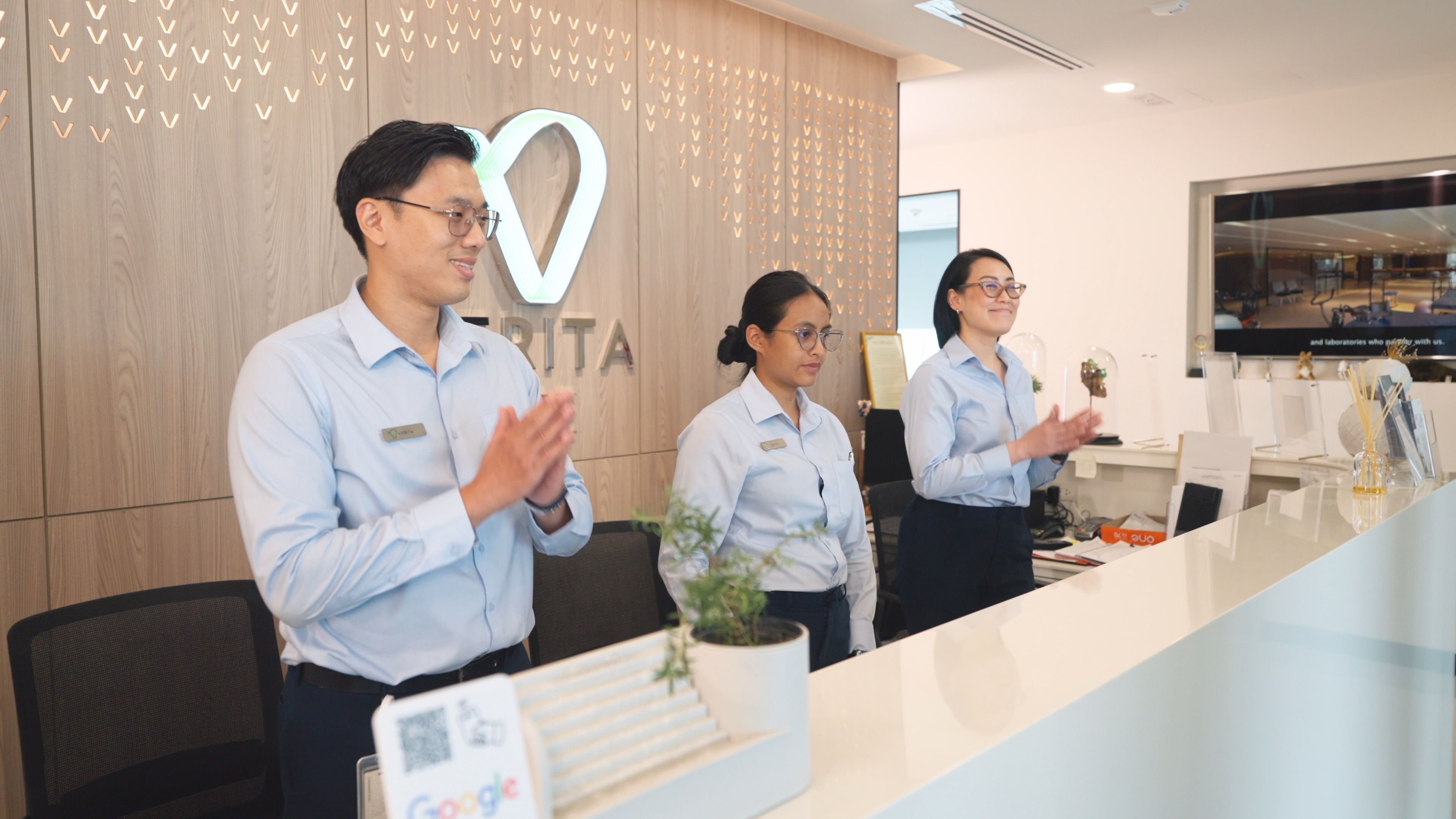 Three members of staff behind a desk and in front of the Verita Life logo, and a further member of staff standing next to the patient, welcome a patient to Verita Life.