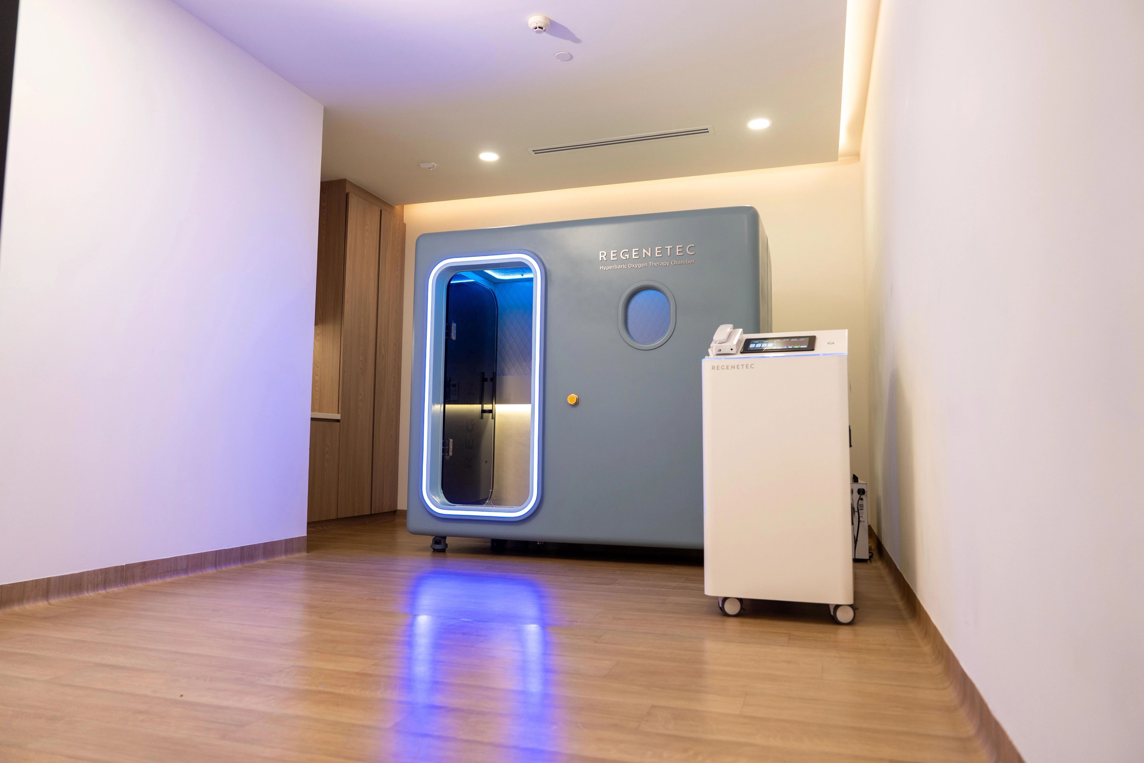 Blue HBOT machine with lights around the door and a small window, inside a room at a medical facility.