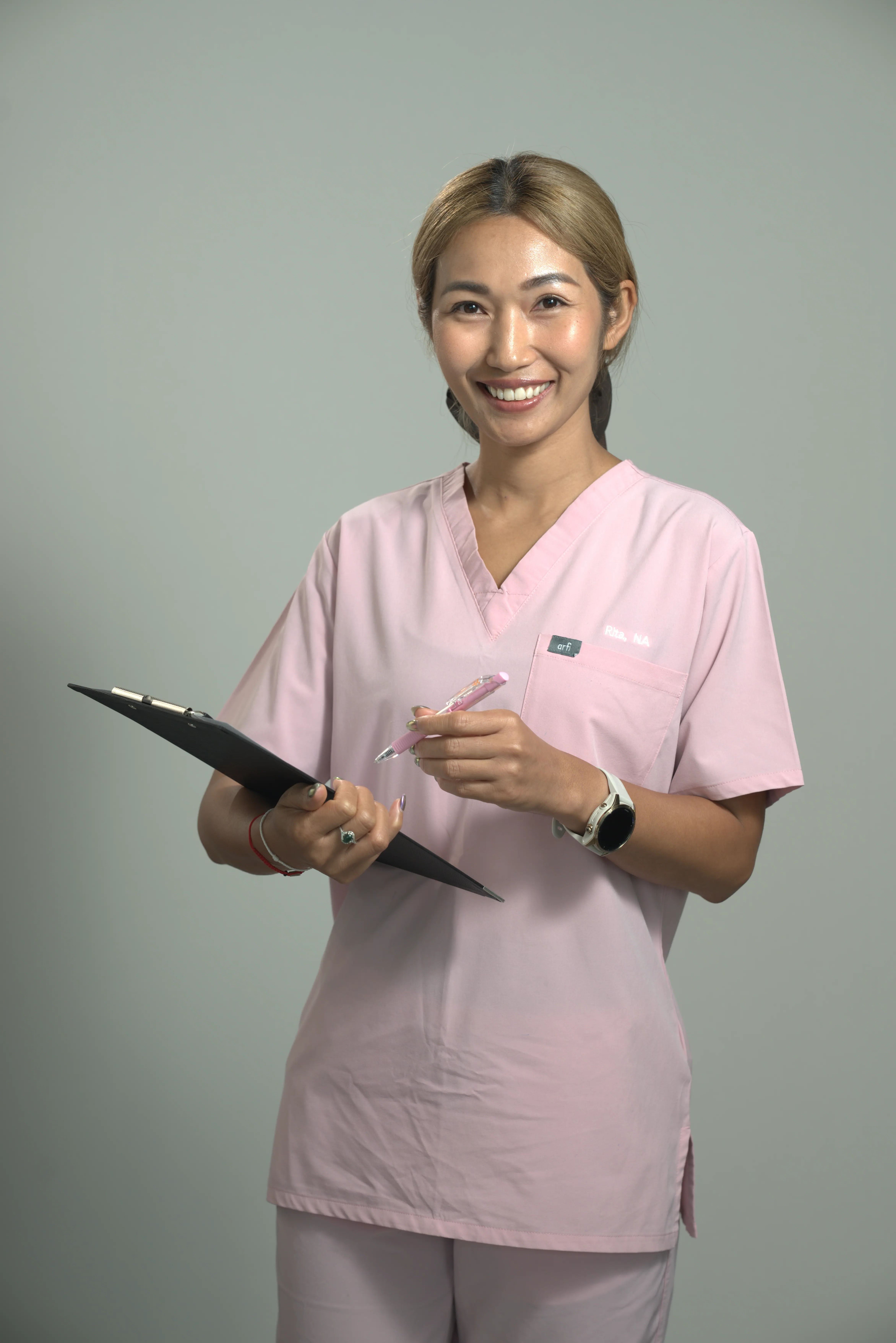 Smiling lady in a pink nurses outfit holding a clipboard