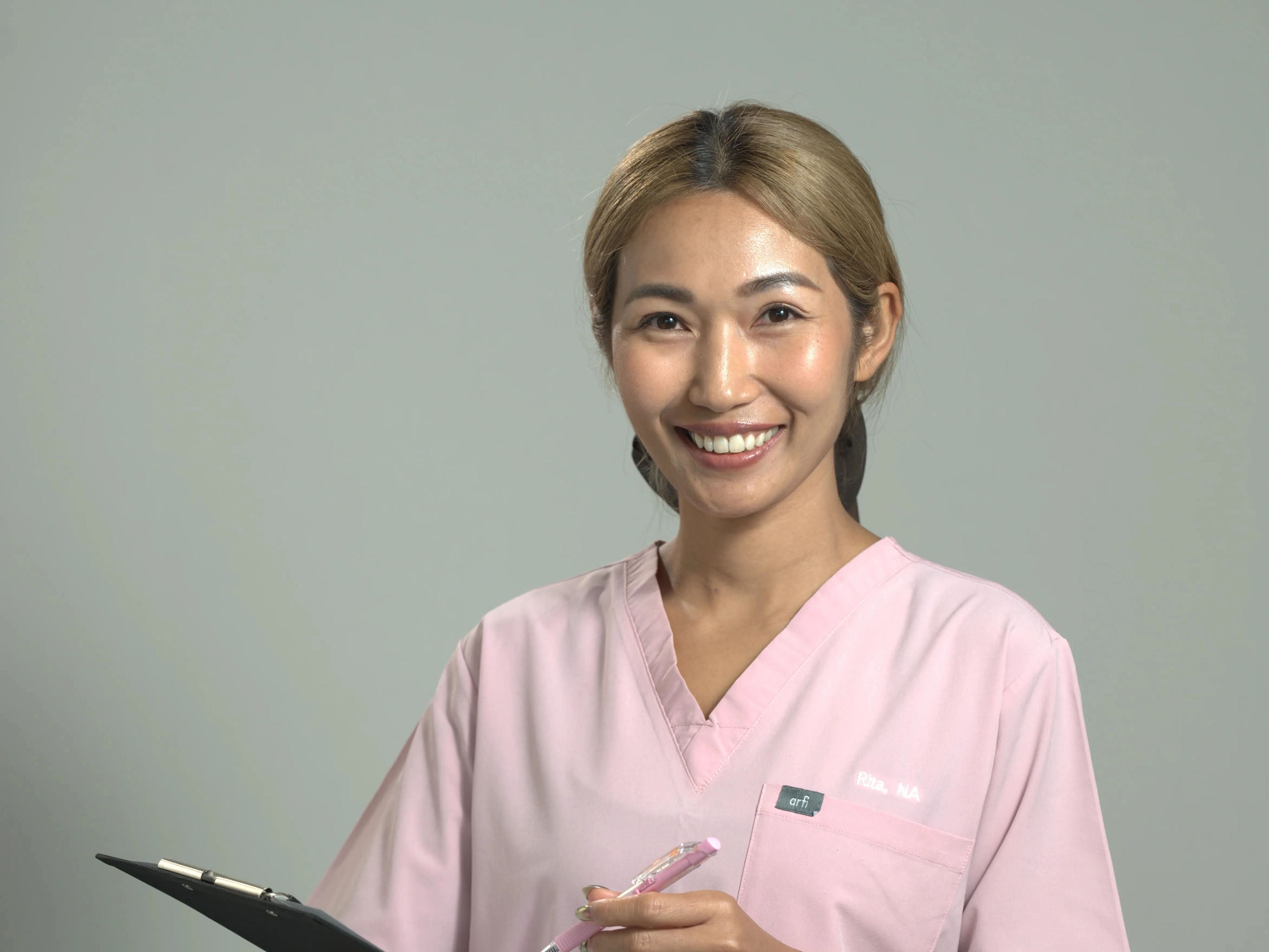 Smiling lady in a pink nurses outfit holding a clipboard