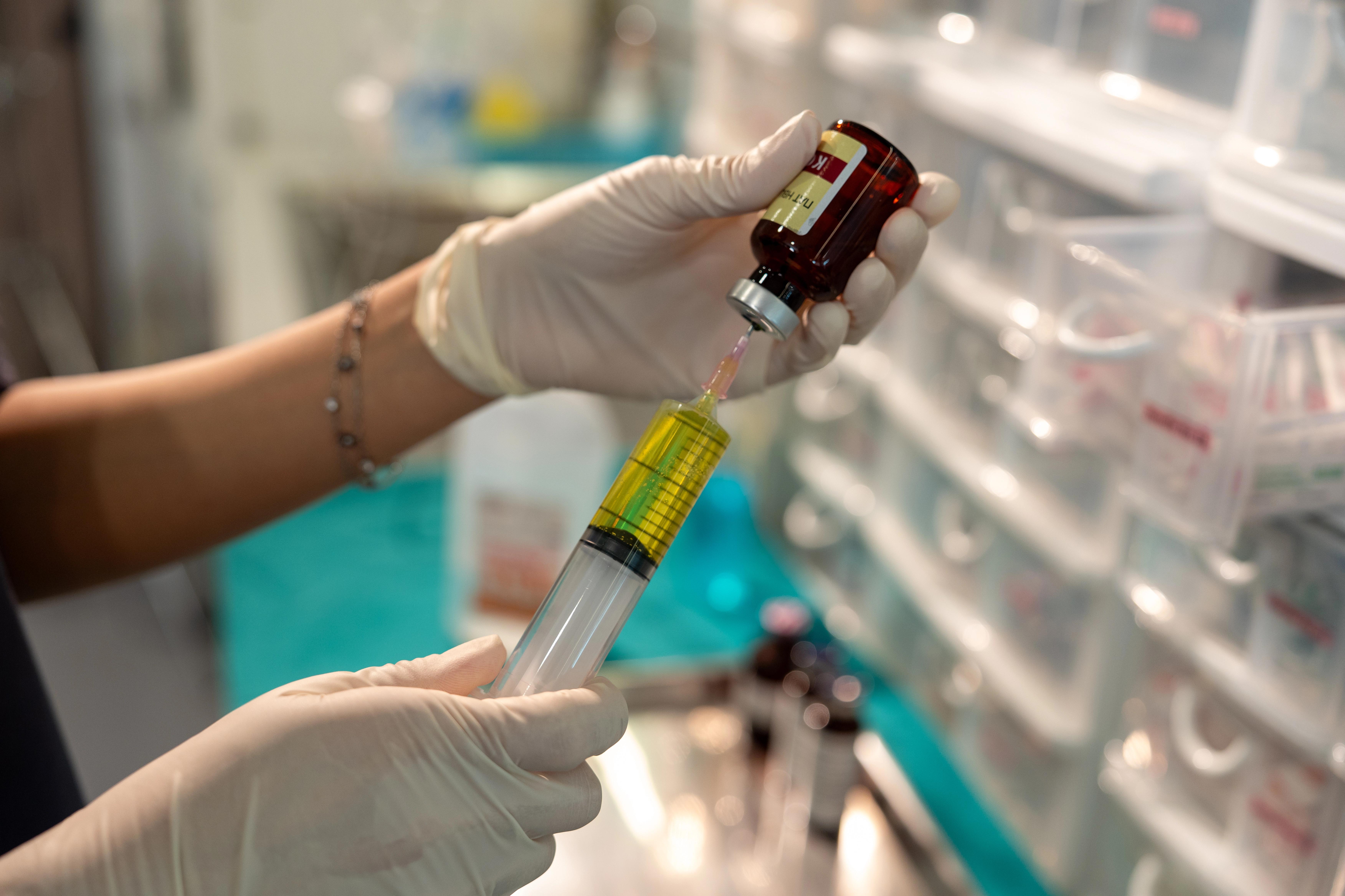 medical professional fills a syringe through a needle into a small glass pot of medicine.