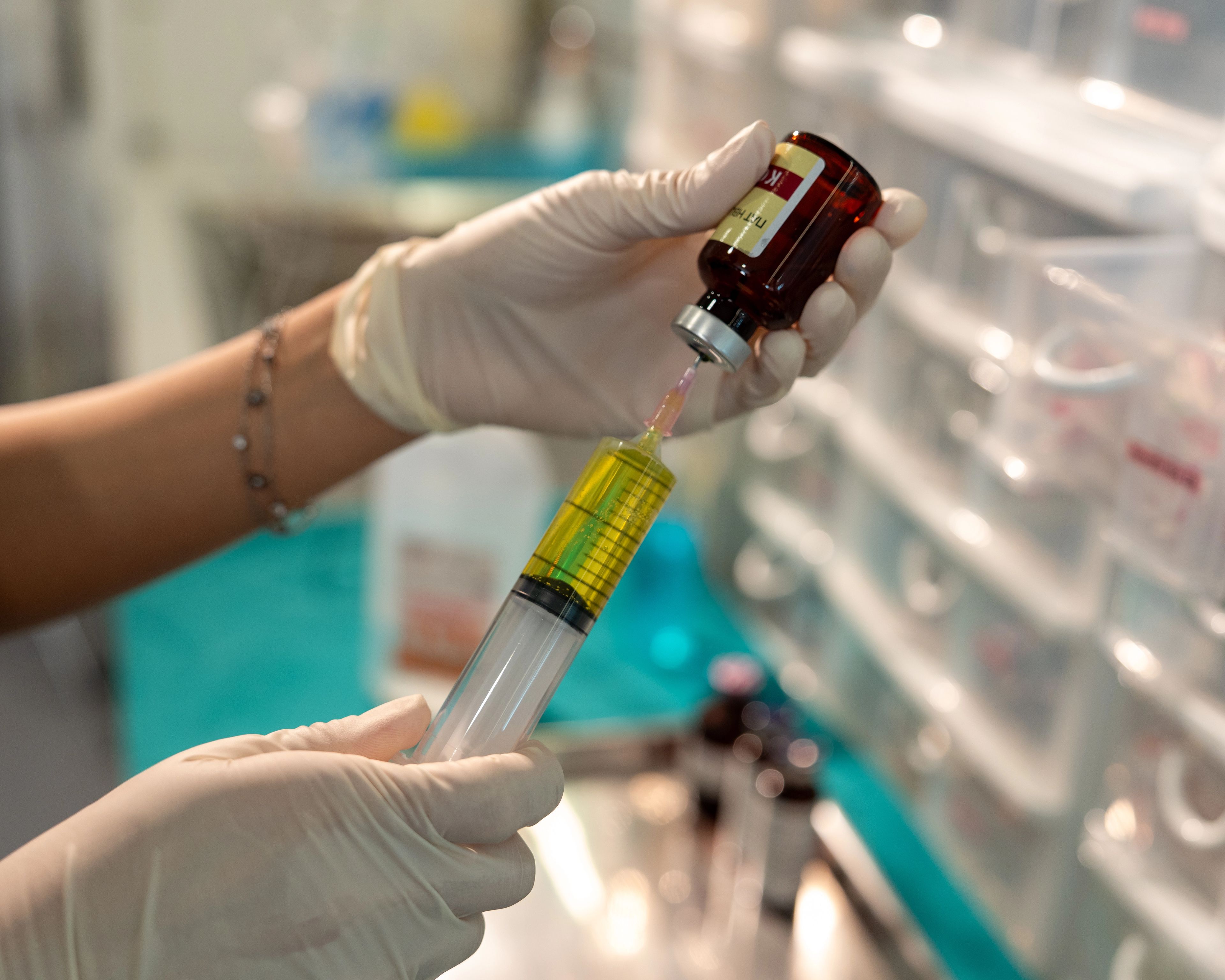 medical professional fills a syringe through a needle into a small glass pot of medicine.