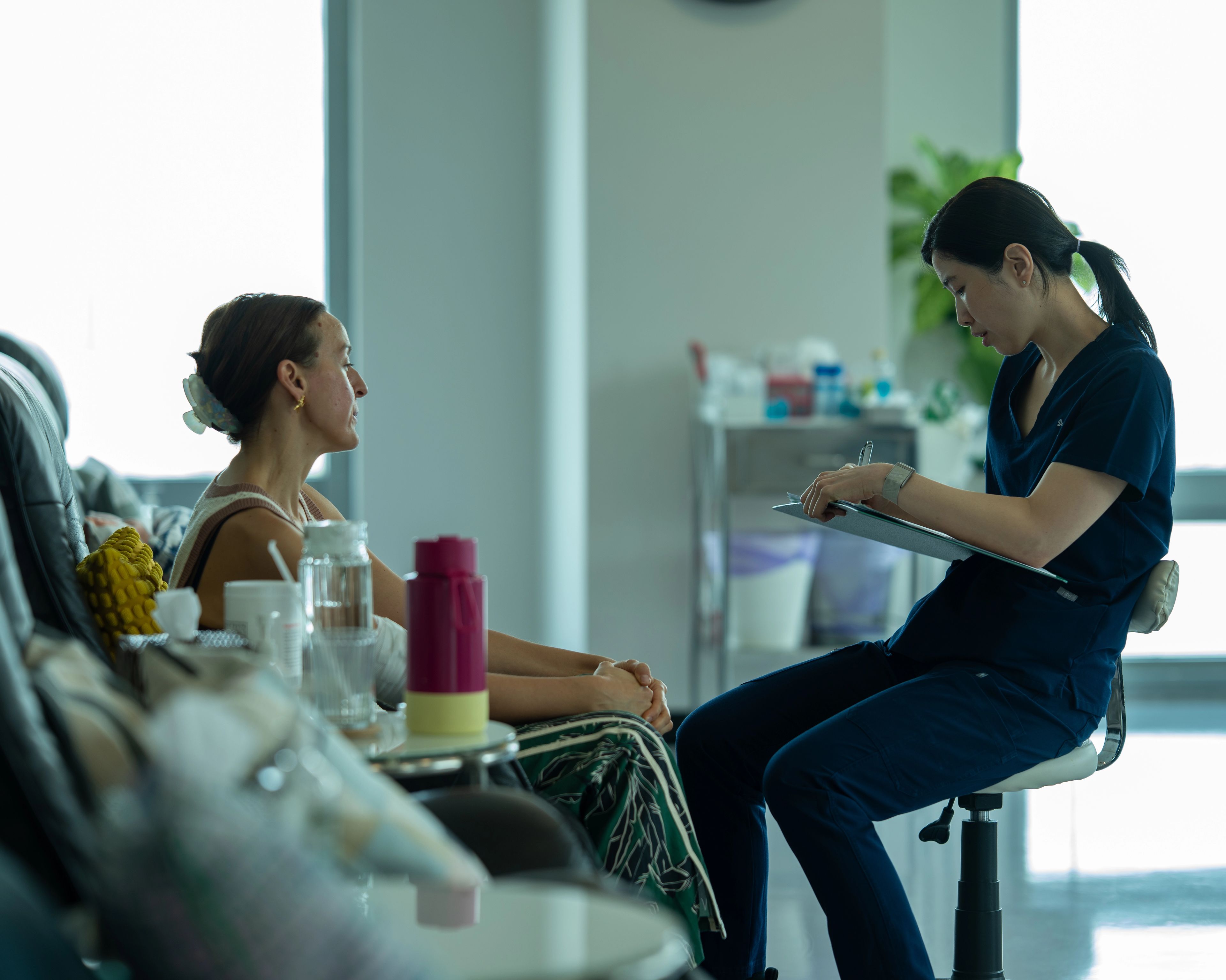 Patient sits in a black leather chair having a conversation with a medical professional in scrubs who is sitting in front of her.